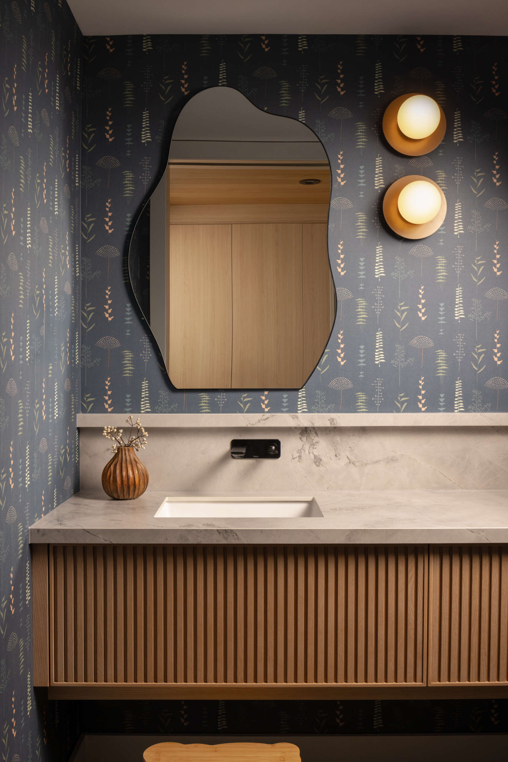 This modern bathroom introduces deep blue wallpaper with a botanical print as a counterpoint to the otherwise minimal palette, adding warmth and individuality.