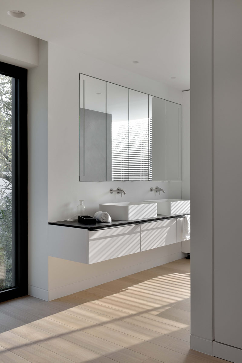 In the bathroom, dual sinks sit beneath oversized mirrors. Wooden floors add warmth, balancing the modern palette and bringing comfort to the daily routine.