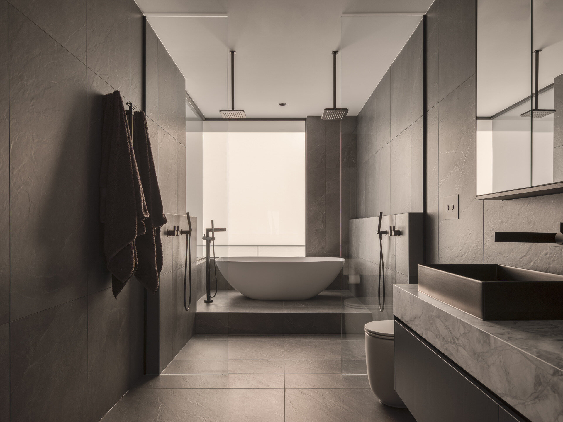 In this bathroom, large format grey tiles covers the walls and floor, while the bathtub is raised up on a platform.
