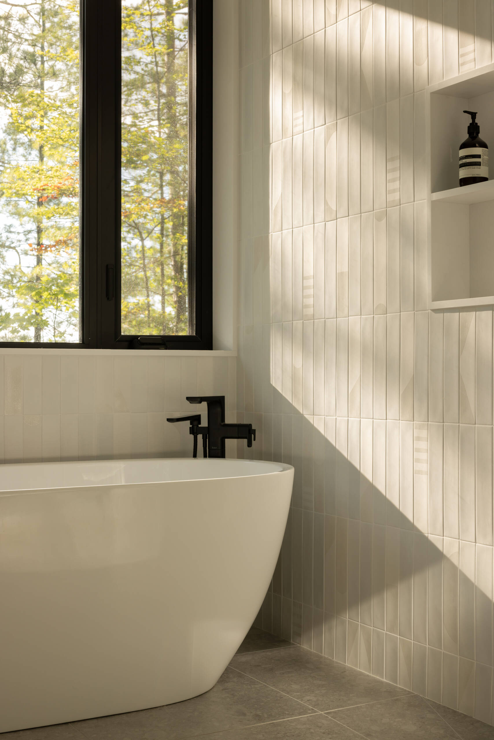 In this modern bathroom, a palette of white tiles and light wood brightens the space, underscoring the interior’s balance of contrast. The finish creates a clean, light-filled atmosphere, in dialogue with the natural light that filters through.