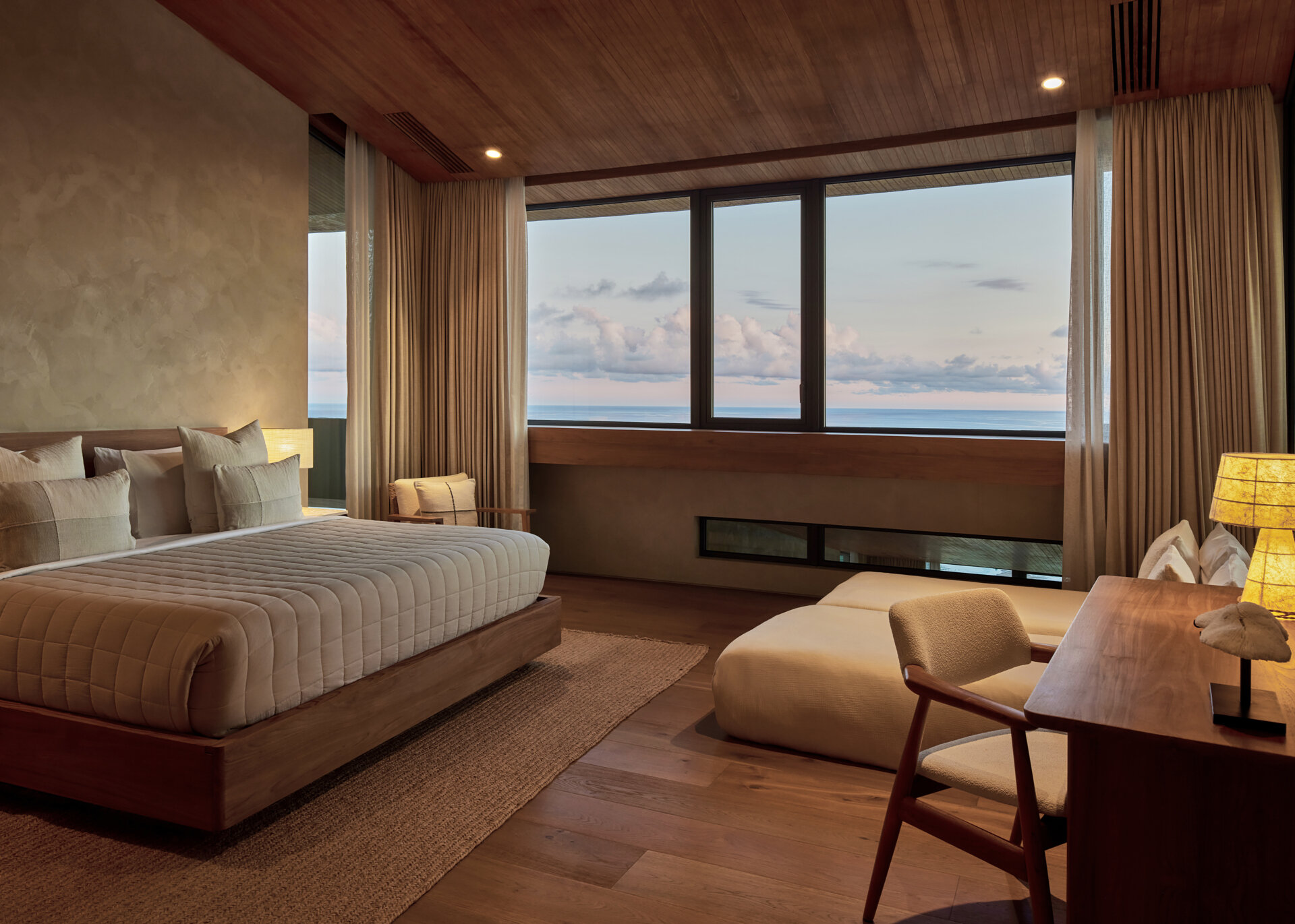 A contemporary bedroom with natural materials, has views of the water.