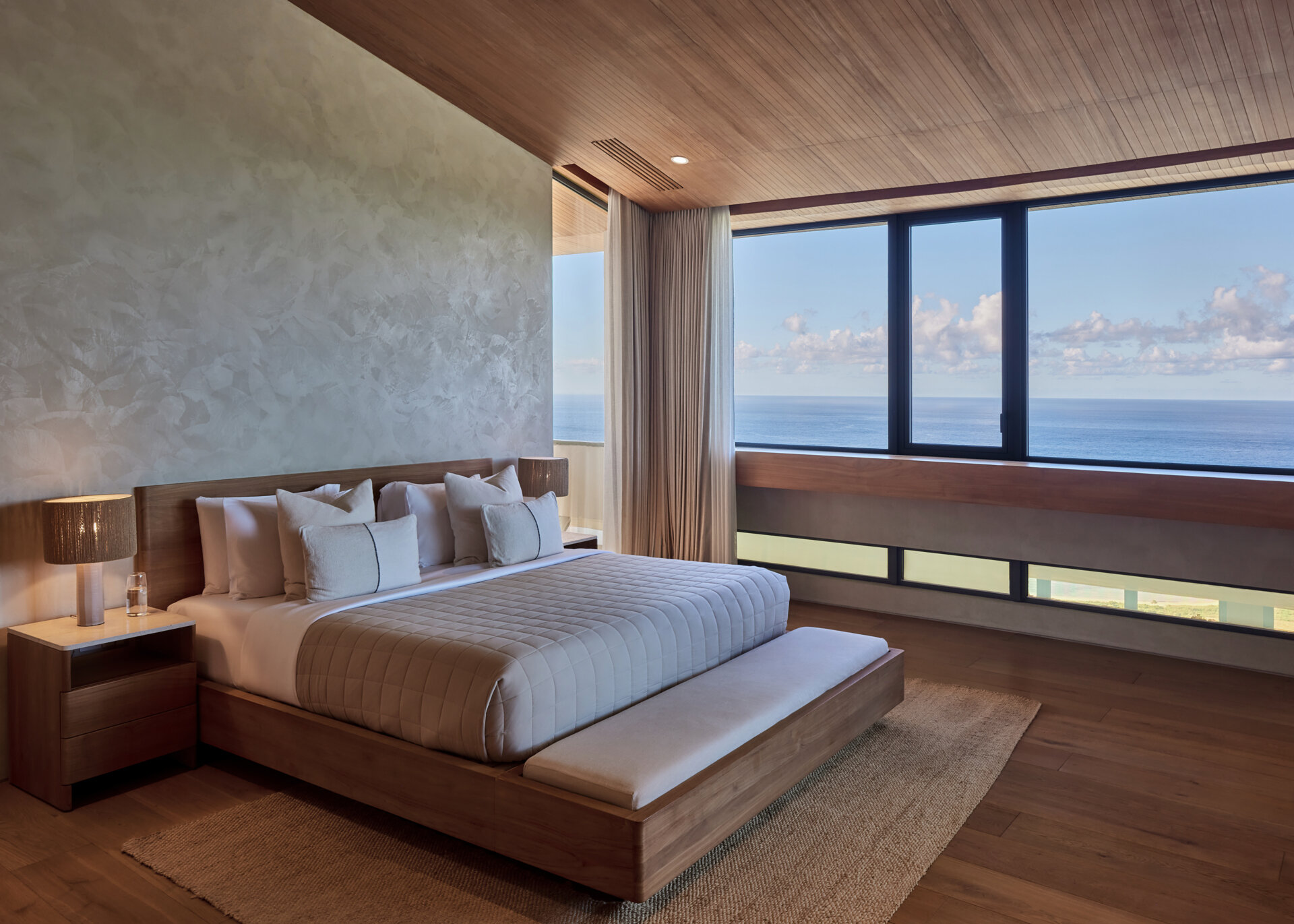 A contemporary bedroom with natural materials, has views of the water.