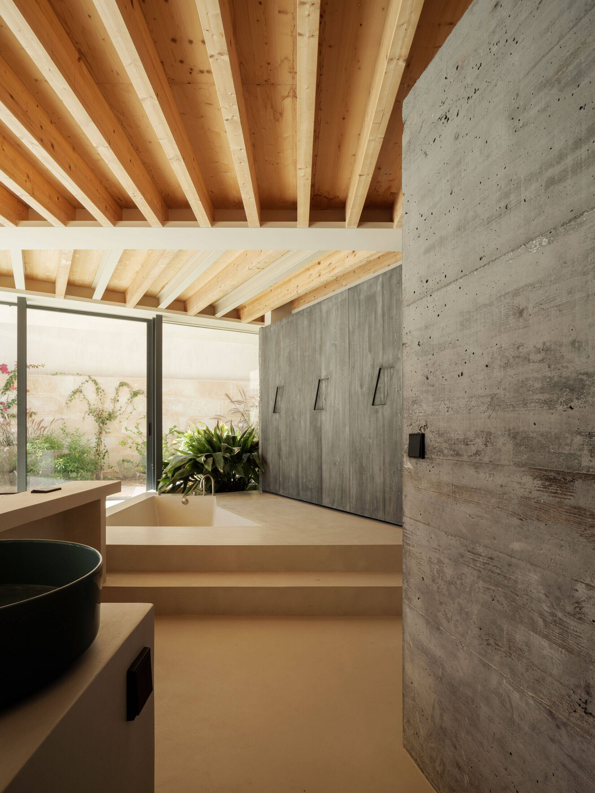 At Can Tudó, the bedrooms flow seamlessly into open bathrooms, with freestanding tubs, sinks, and wardrobes arranged as sculptural dividers. These floating elements define space without enclosing it, allowing every corner to capture uninterrupted views of the bay.