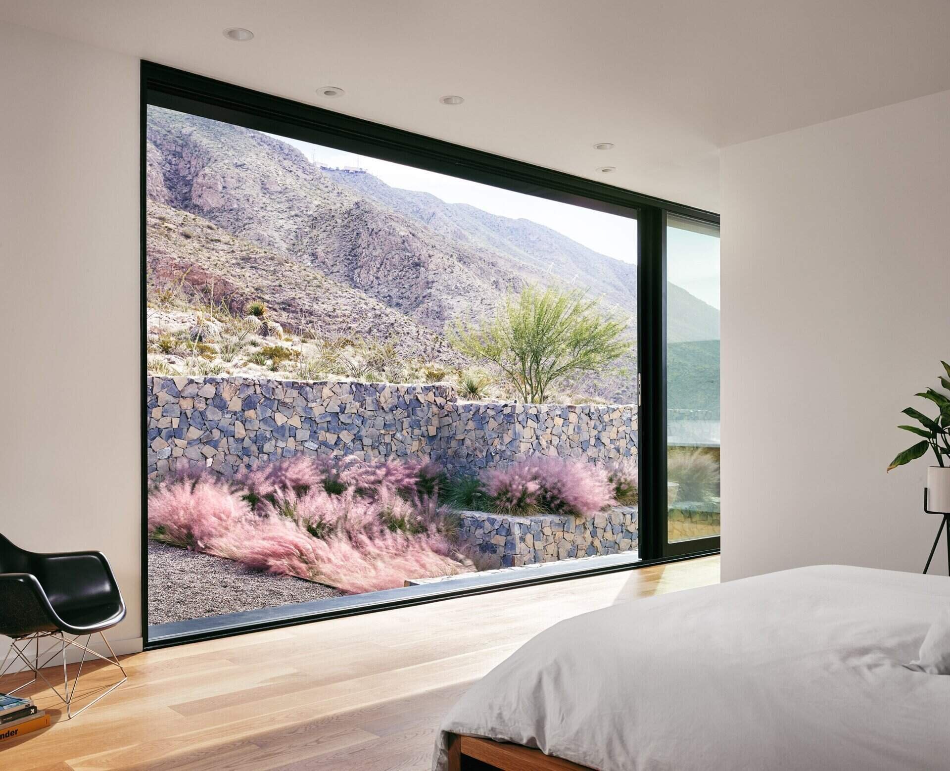 A serene master bedroom with oak finishes and sliding doors to a desert patio inside a modern mountain home.