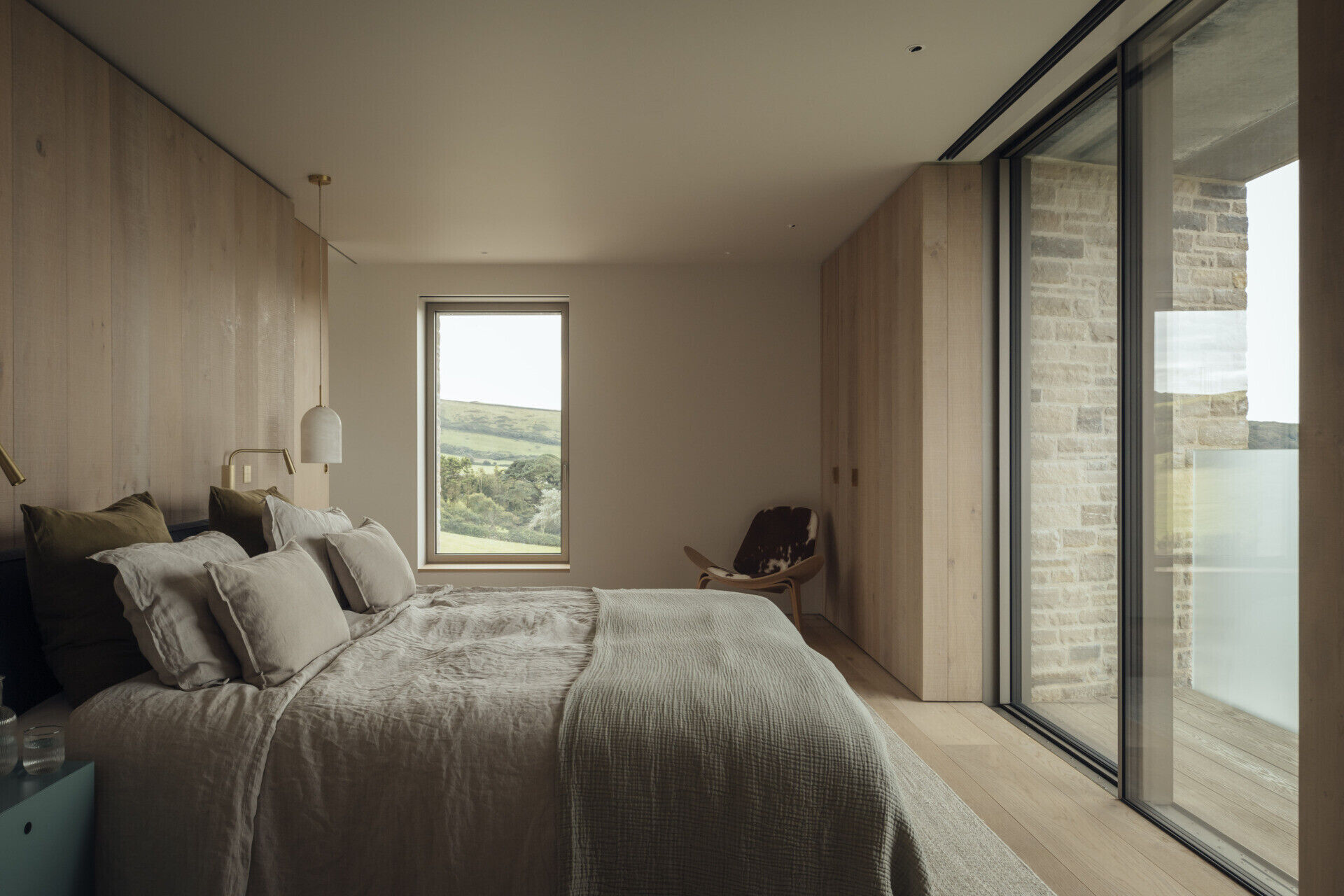 A modern bedroom with a wood accent wall and wardrobe, also includes a window and sliding glass door that opens to a private balcony.