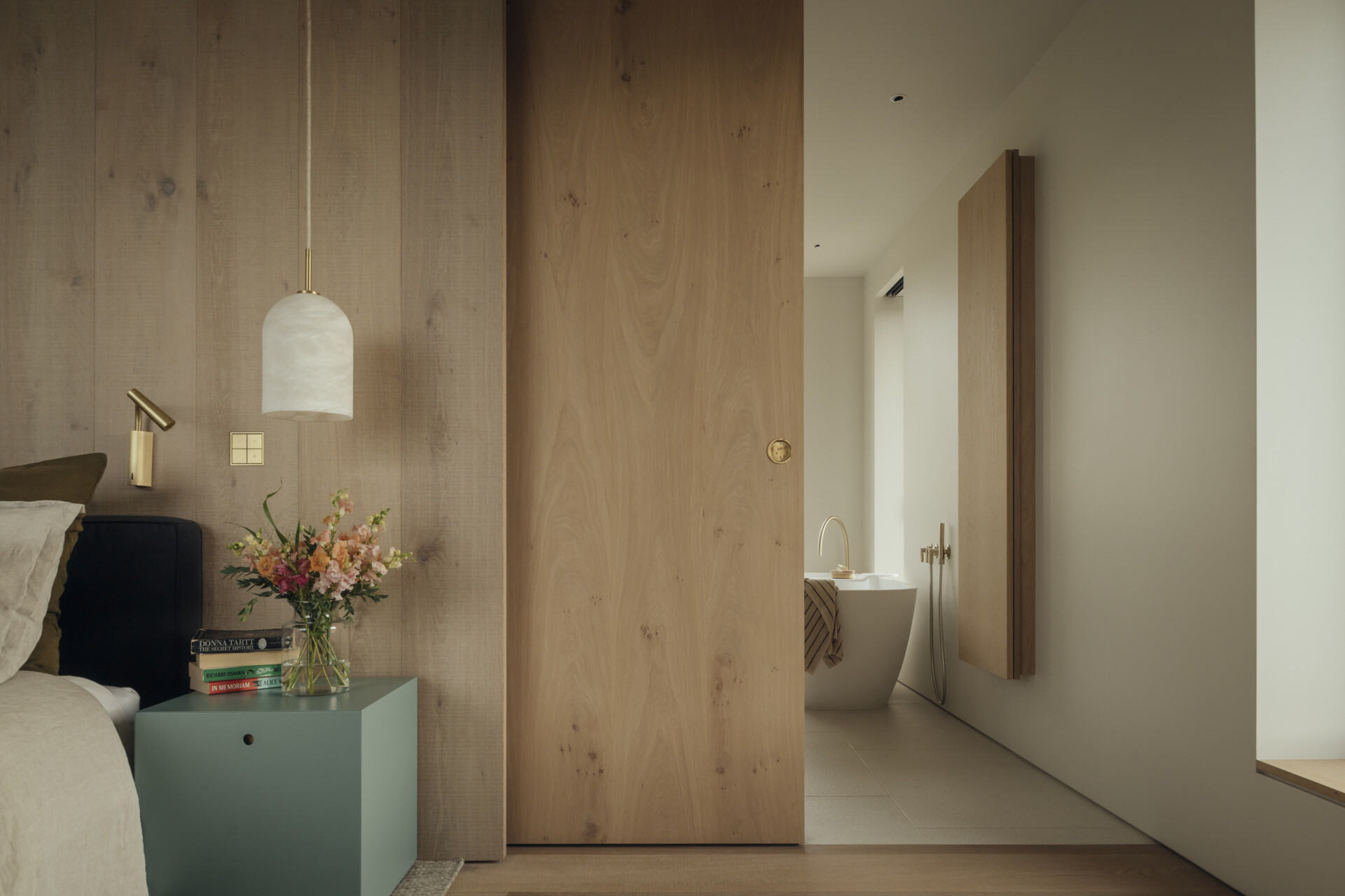 A modern bedroom with a wood accent wall has a sliding door that opens to reveal the ensuite bathroom.