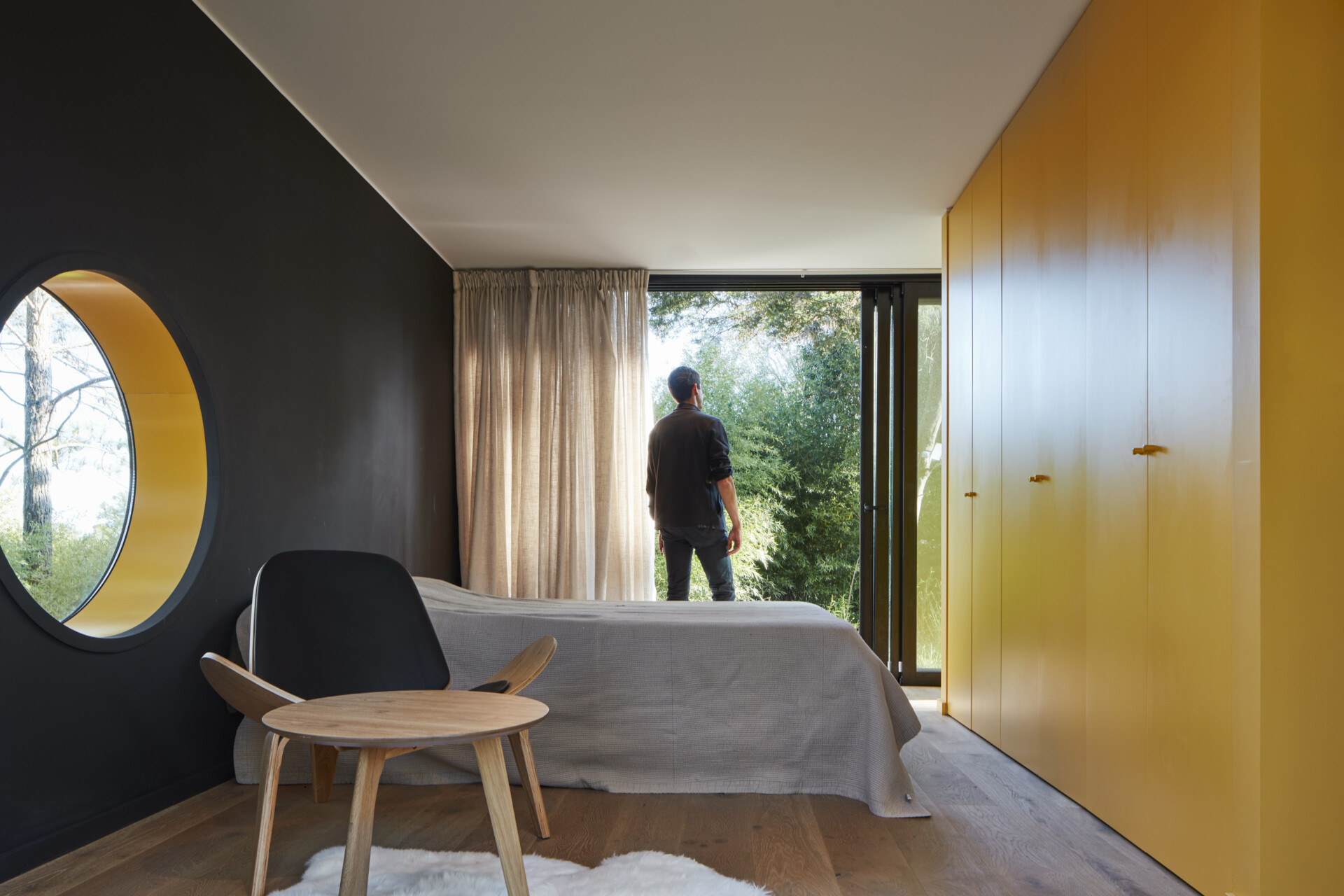 A modern bedroom with a black accent wall, wood floors, and bright yellow closets.