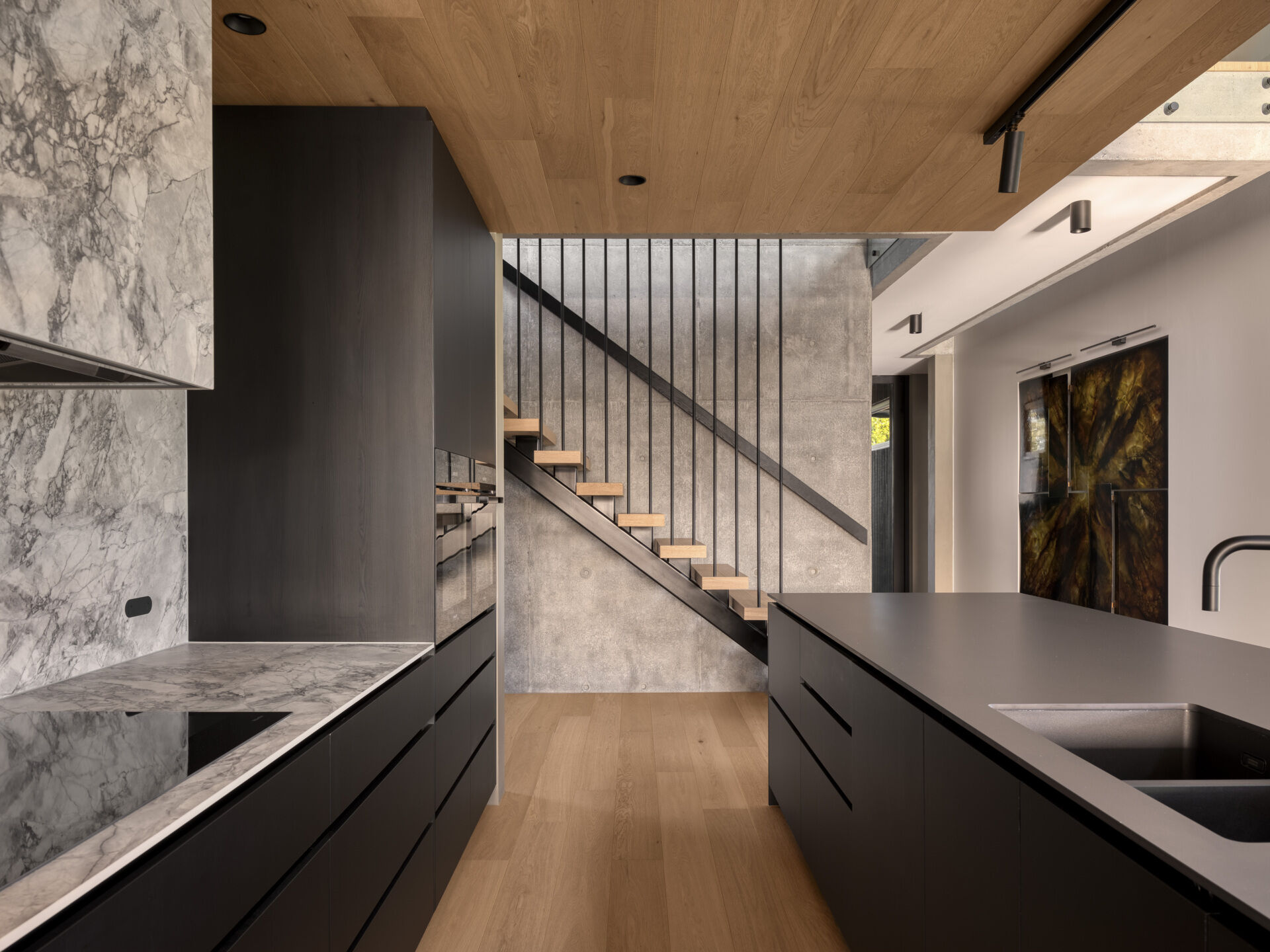 Stepping inside, the kitchen uses black-stained timber, stone, and raw concrete to combine durability with texture. Abundant natural light filters in, connecting the space to the outdoors. Adjacent, the butlers pantry supports storage and preparation, keeping the main kitchen sleek and functional. Both spaces reflect the home’s emphasis on material honesty and subtropical living.