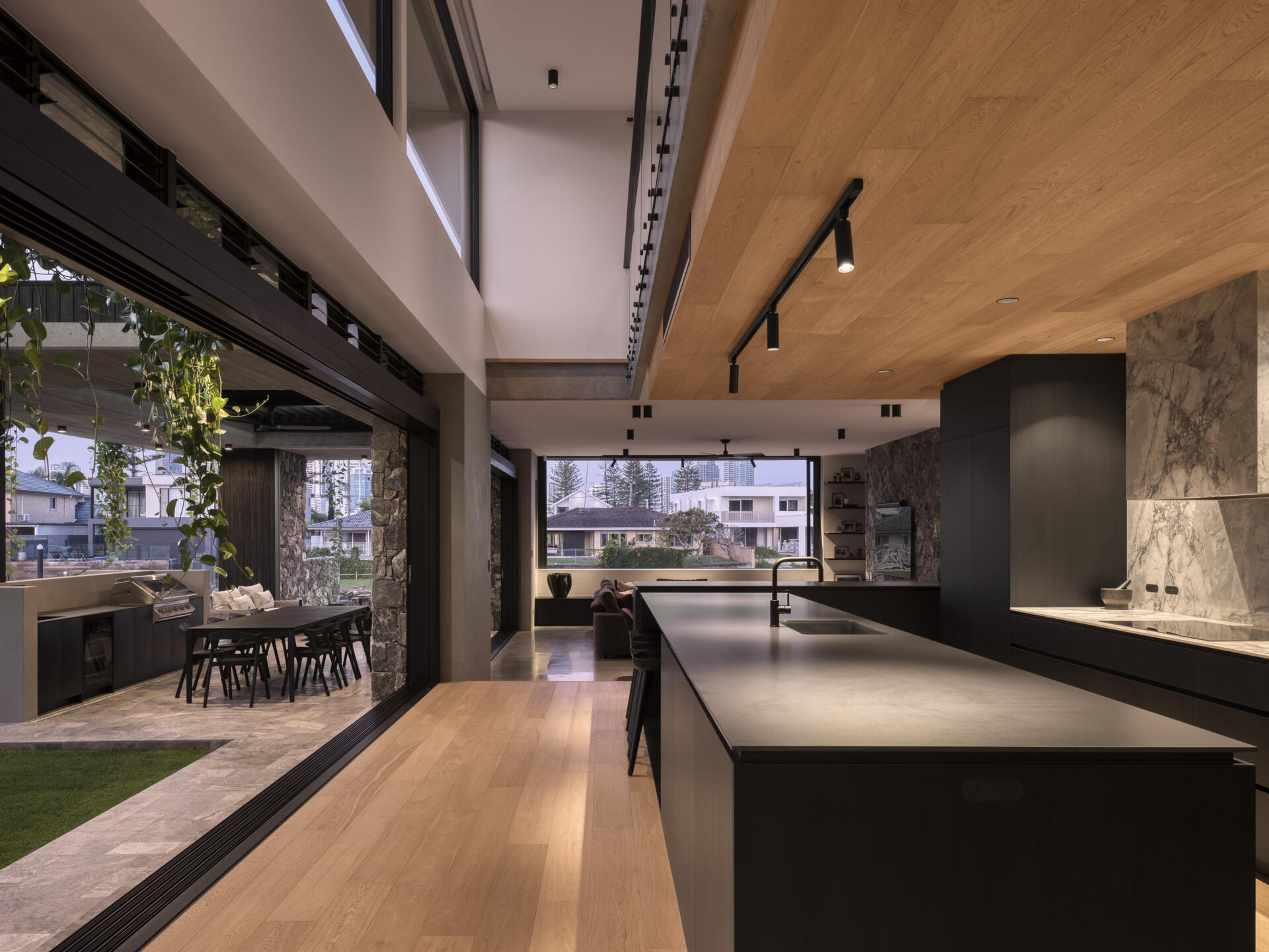 Stepping inside, the kitchen uses black-stained timber, stone, and raw concrete to combine durability with texture. Abundant natural light filters in, connecting the space to the outdoors. Adjacent, the butlers pantry supports storage and preparation, keeping the main kitchen sleek and functional. Both spaces reflect the home’s emphasis on material honesty and subtropical living.