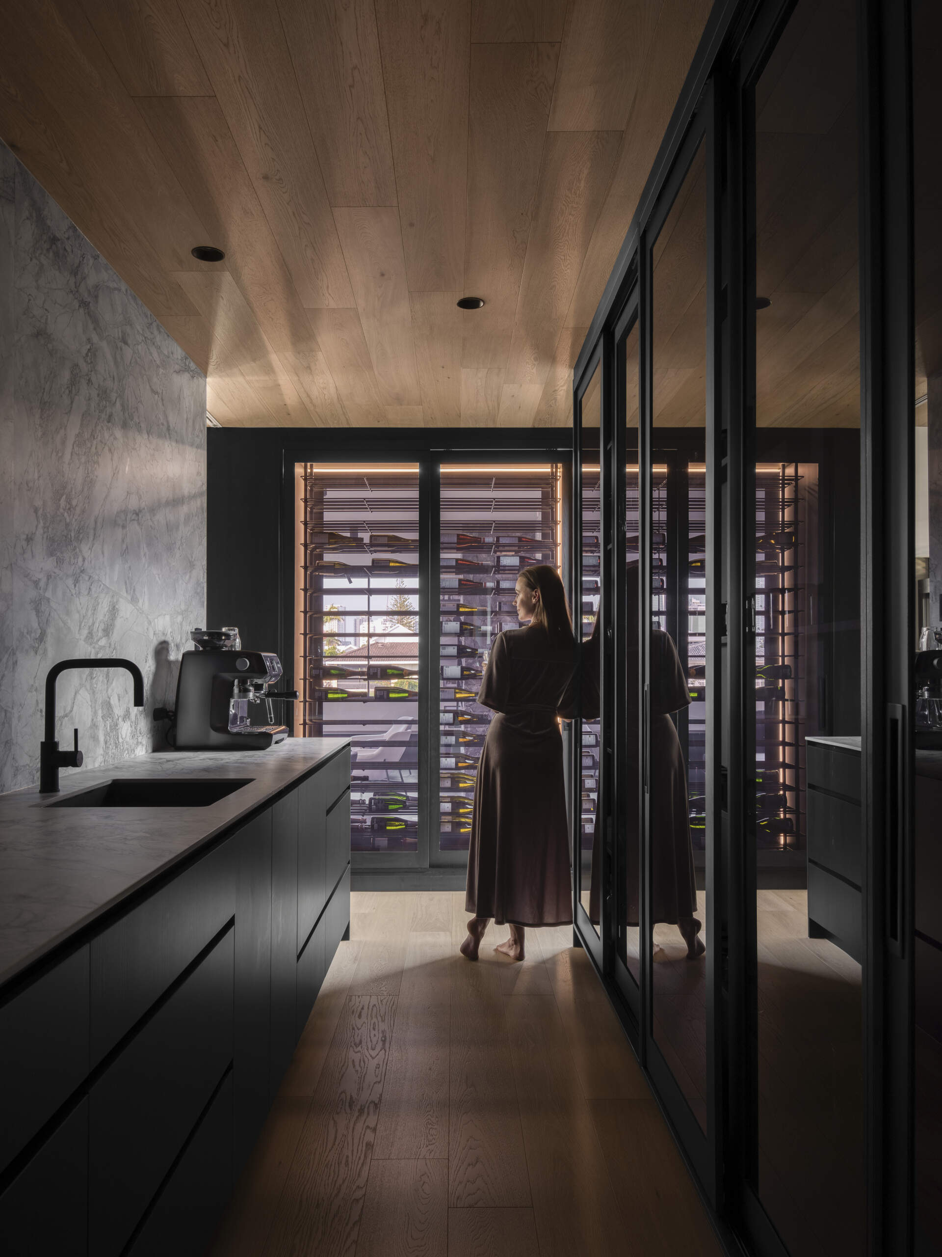 Stepping inside, the kitchen uses black-stained timber, stone, and raw concrete to combine durability with texture. Abundant natural light filters in, connecting the space to the outdoors. Adjacent, the butlers pantry supports storage and preparation, keeping the main kitchen sleek and functional. Both spaces reflect the home’s emphasis on material honesty and subtropical living.