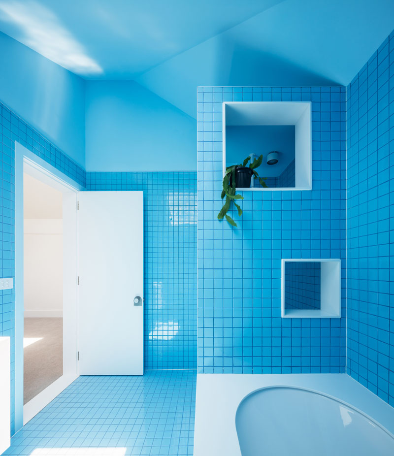 This bathroom bursts with bright blue, creating a bold monochrome environment. Thoughtful cut-outs in the wall beside the tub keep essentials organized and within reach, making it both functional and fun.