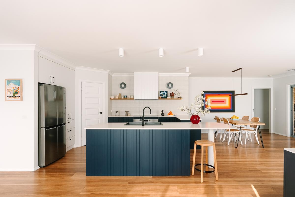 Removing a wall opened this remodeled kitchen to the dining and living areas. Custom royal blue joinery, a central island, and layered lighting created a bold, flexible kitchen hub.