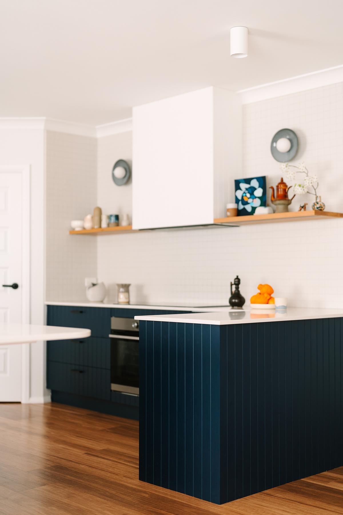 Removing a wall opened this remodeled kitchen to the dining and living areas. Custom royal blue joinery, a central island, and layered lighting created a bold, flexible kitchen hub.