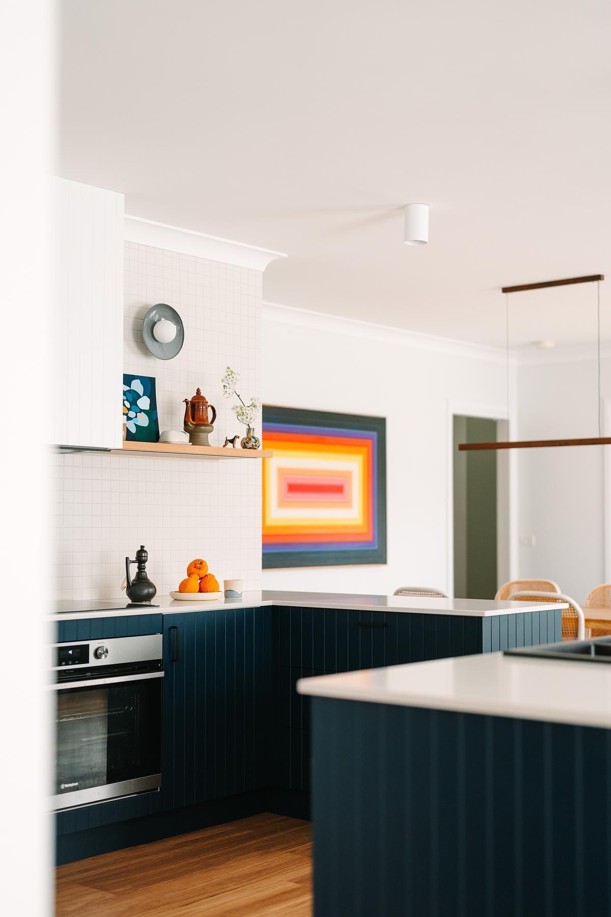 Removing a wall opened this remodeled kitchen to the dining and living areas. Custom royal blue joinery, a central island, and layered lighting created a bold, flexible kitchen hub.