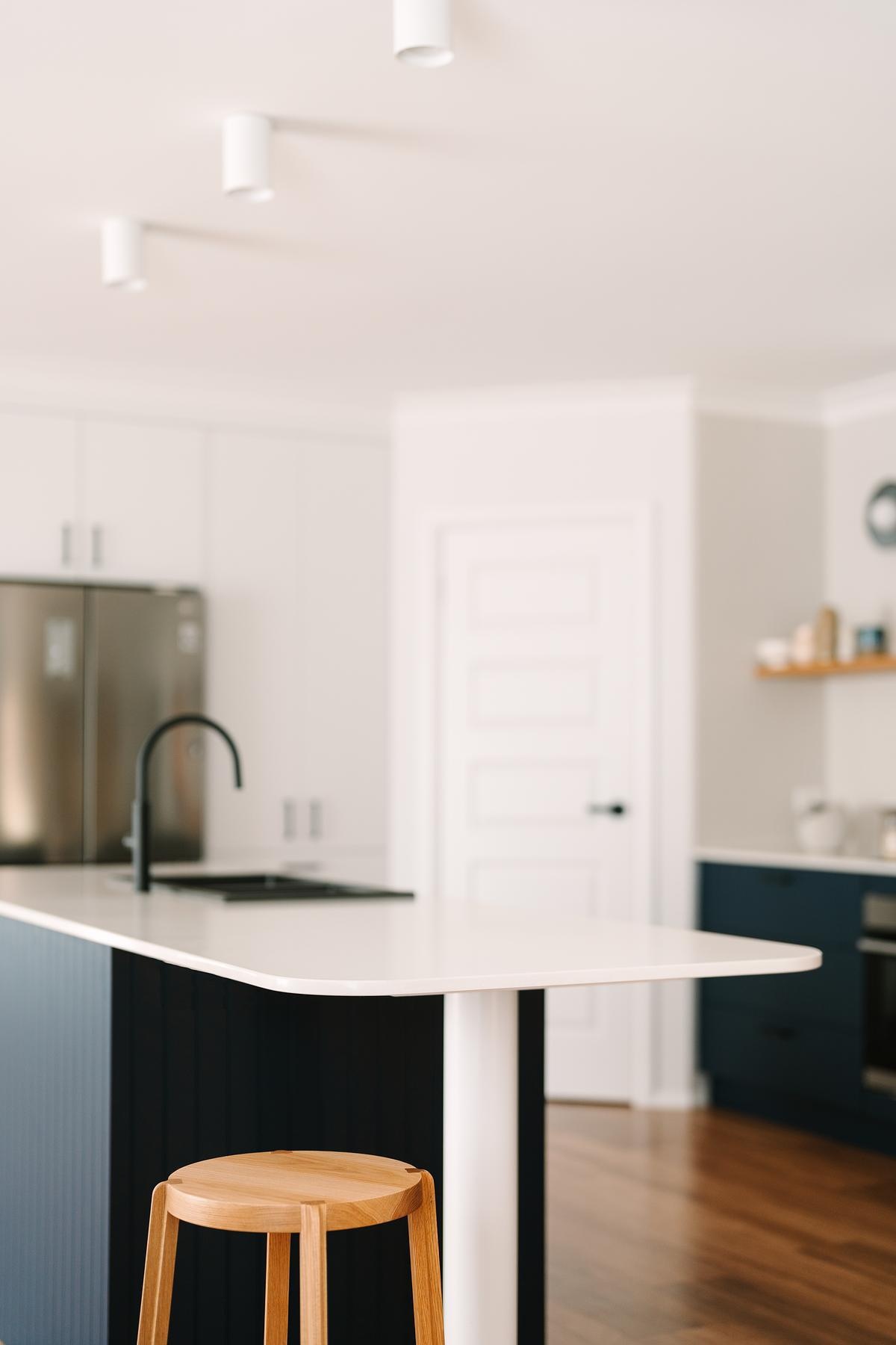 Removing a wall opened this remodeled kitchen to the dining and living areas. Custom royal blue joinery, a central island, and layered lighting created a bold, flexible kitchen hub.