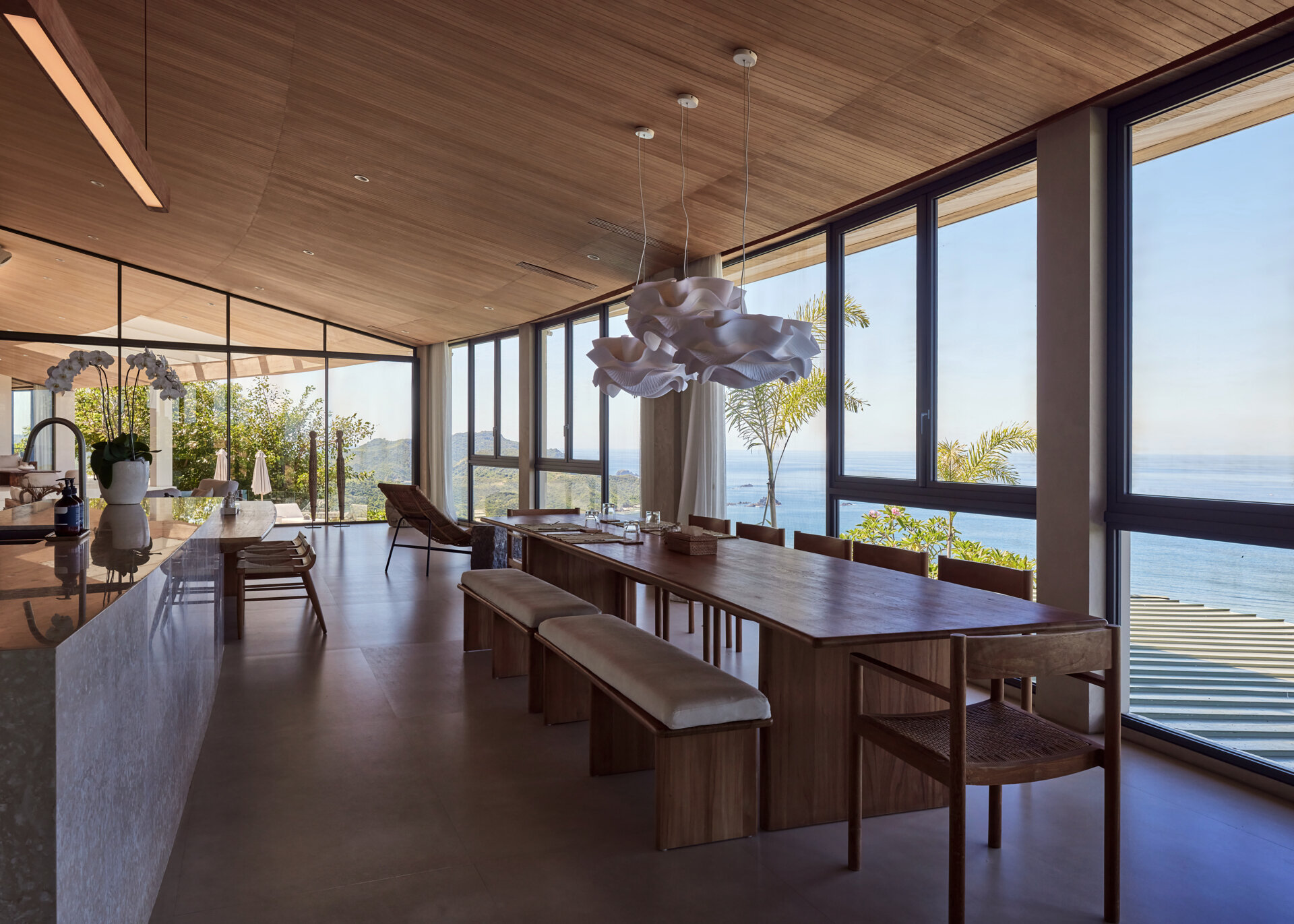 The social areas open up after the entry, bringing together the living room, dining room, and kitchen. Walls of windows fills the interior with an abundance of natural light, while the wood ceiling and furniture adds warmth to the home.
