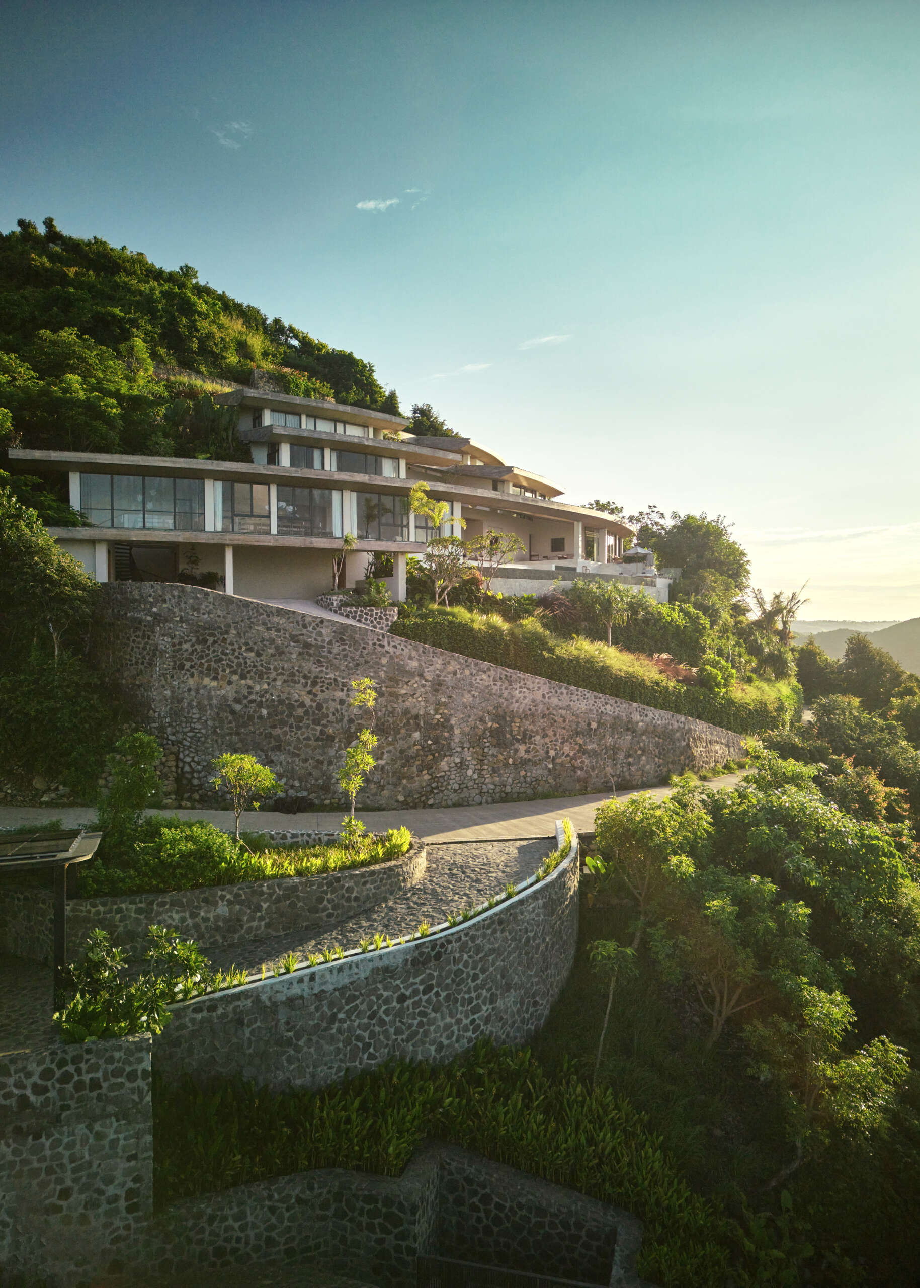 The home’s design is guided by the terrain. Its vertical layout adapts to the steep hillside, stacking functions across several levels. The geometry is based on concentric circles and radial segments, allowing the roofs and volumes to orient naturally with the hilltop.