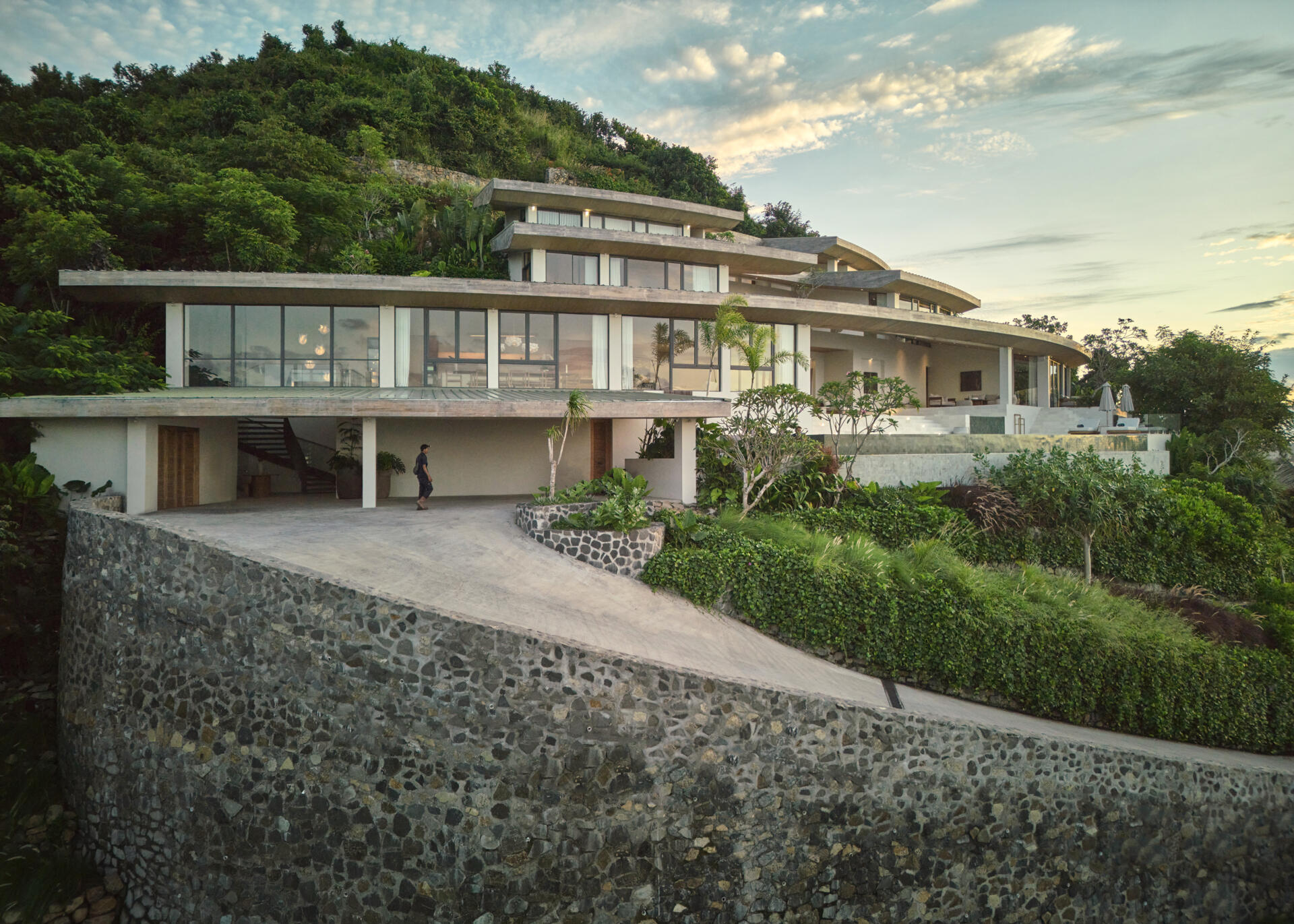 The home’s design is guided by the terrain. Its vertical layout adapts to the steep hillside, stacking functions across several levels. The geometry is based on concentric circles and radial segments, allowing the roofs and volumes to orient naturally with the hilltop.