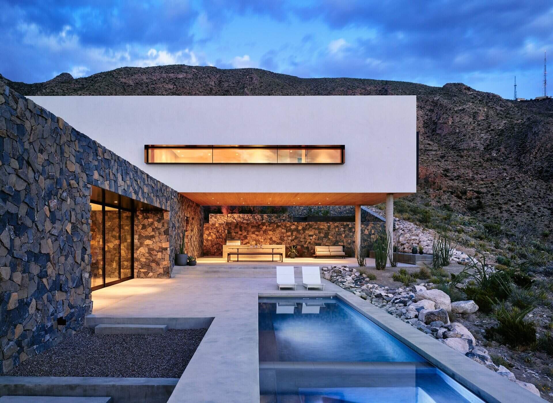 A modern mountain home with a covered outdoor space, pool, and stone walls that blend seamlessly into the Franklin Mountains.