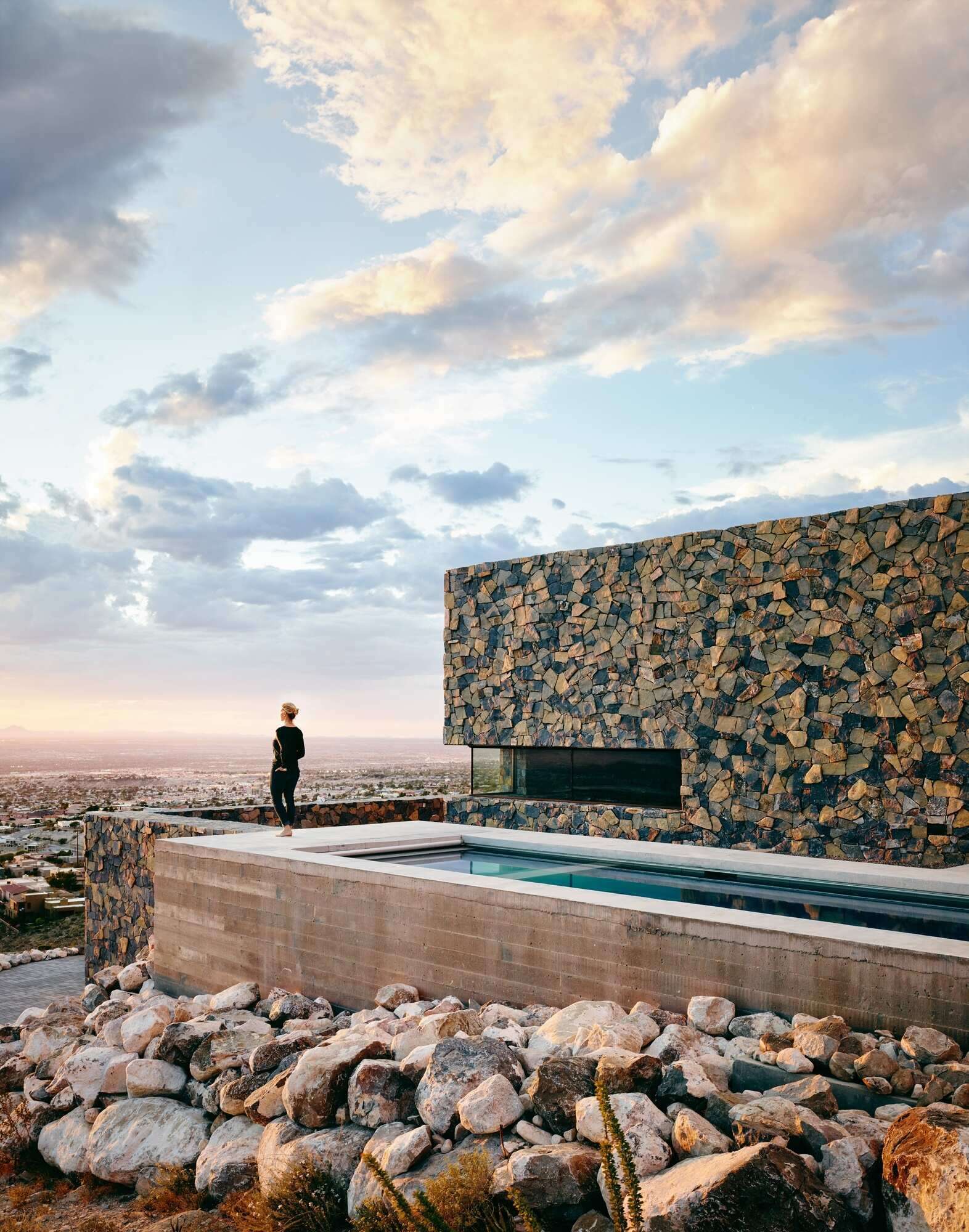 A modern mountain home with a covered outdoor space, pool, and stone walls that blend seamlessly into the Franklin Mountains.