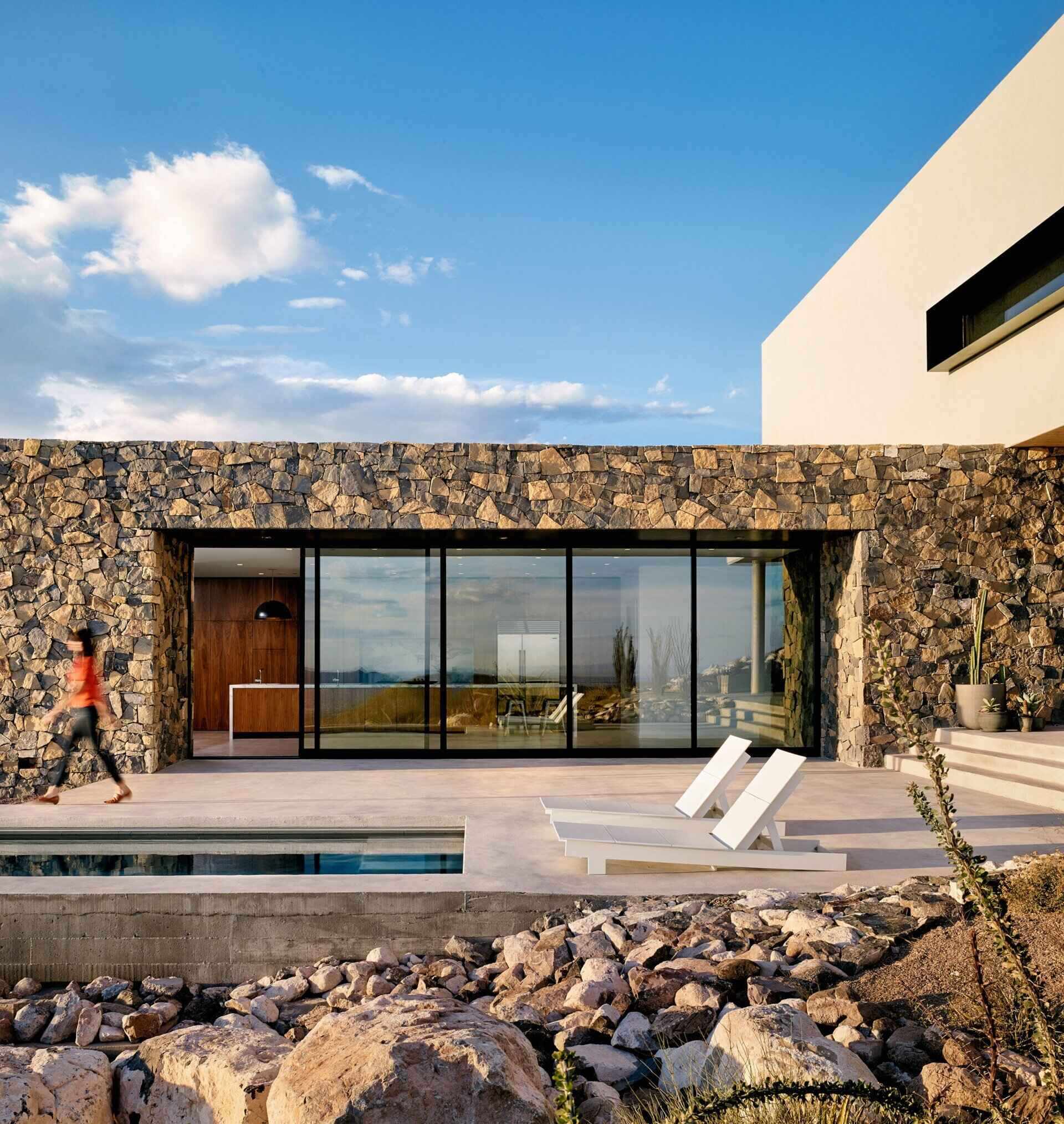 A modern mountain home with a covered outdoor space, pool, and stone walls that blend seamlessly into the Franklin Mountains.