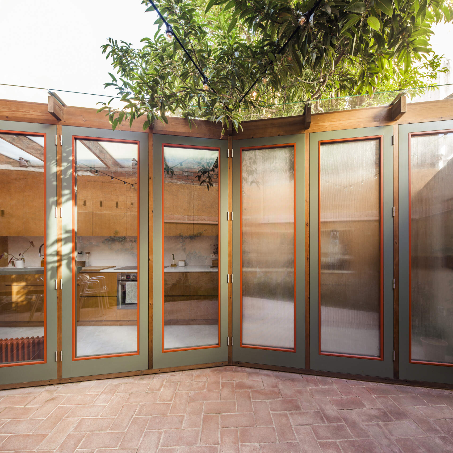This house extension is conceived almost entirely as a transparent structure, built with wood and glass in the spirit of a greenhouse. Rather than blocking light, the glazed facade ensures that natural illumination continues to filter through the rest of the ground floor.