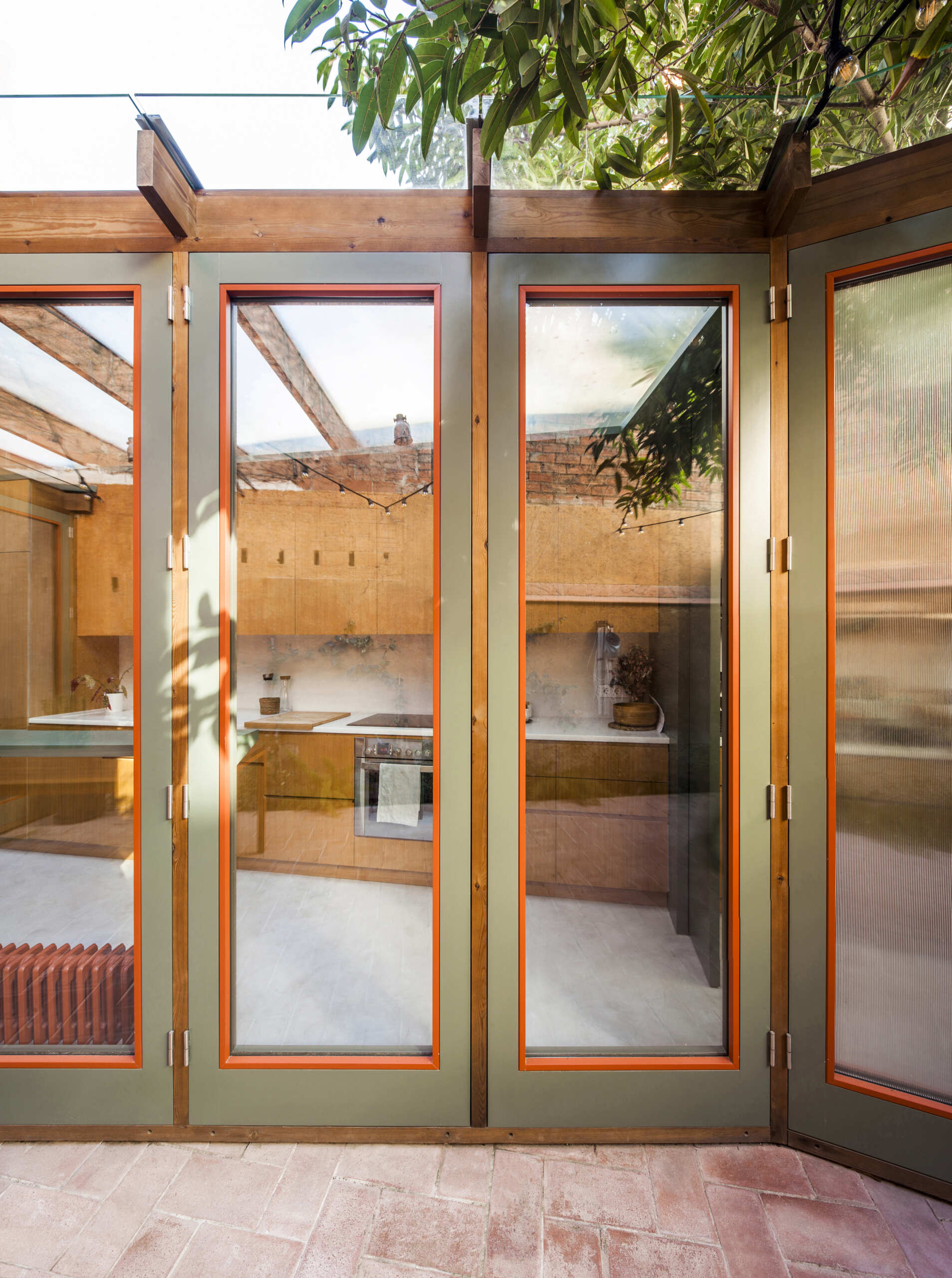 This house extension is conceived almost entirely as a transparent structure, built with wood and glass in the spirit of a greenhouse. Rather than blocking light, the glazed facade ensures that natural illumination continues to filter through the rest of the ground floor.