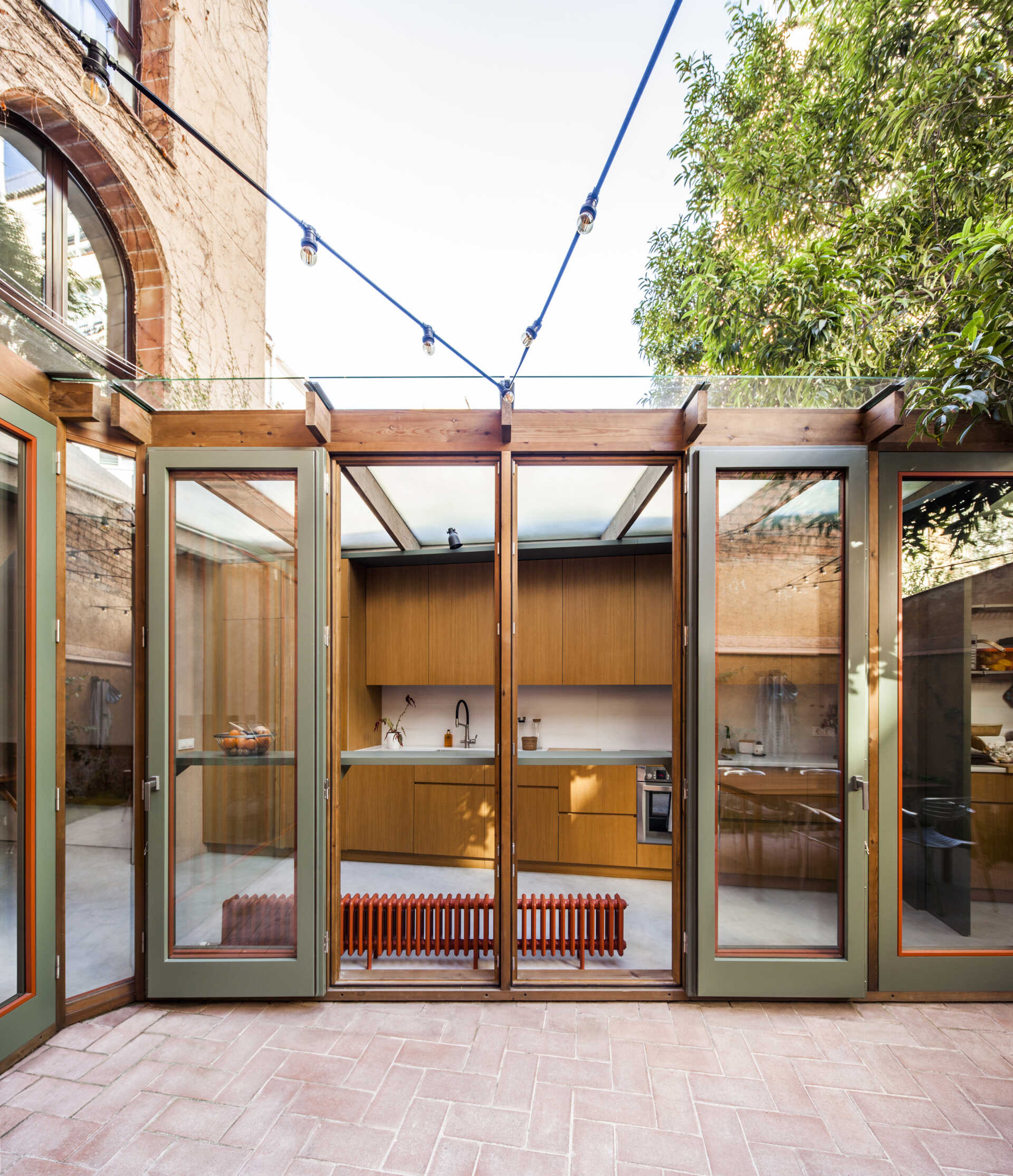 This house extension is conceived almost entirely as a transparent structure, built with wood and glass in the spirit of a greenhouse. Rather than blocking light, the glazed facade ensures that natural illumination continues to filter through the rest of the ground floor.