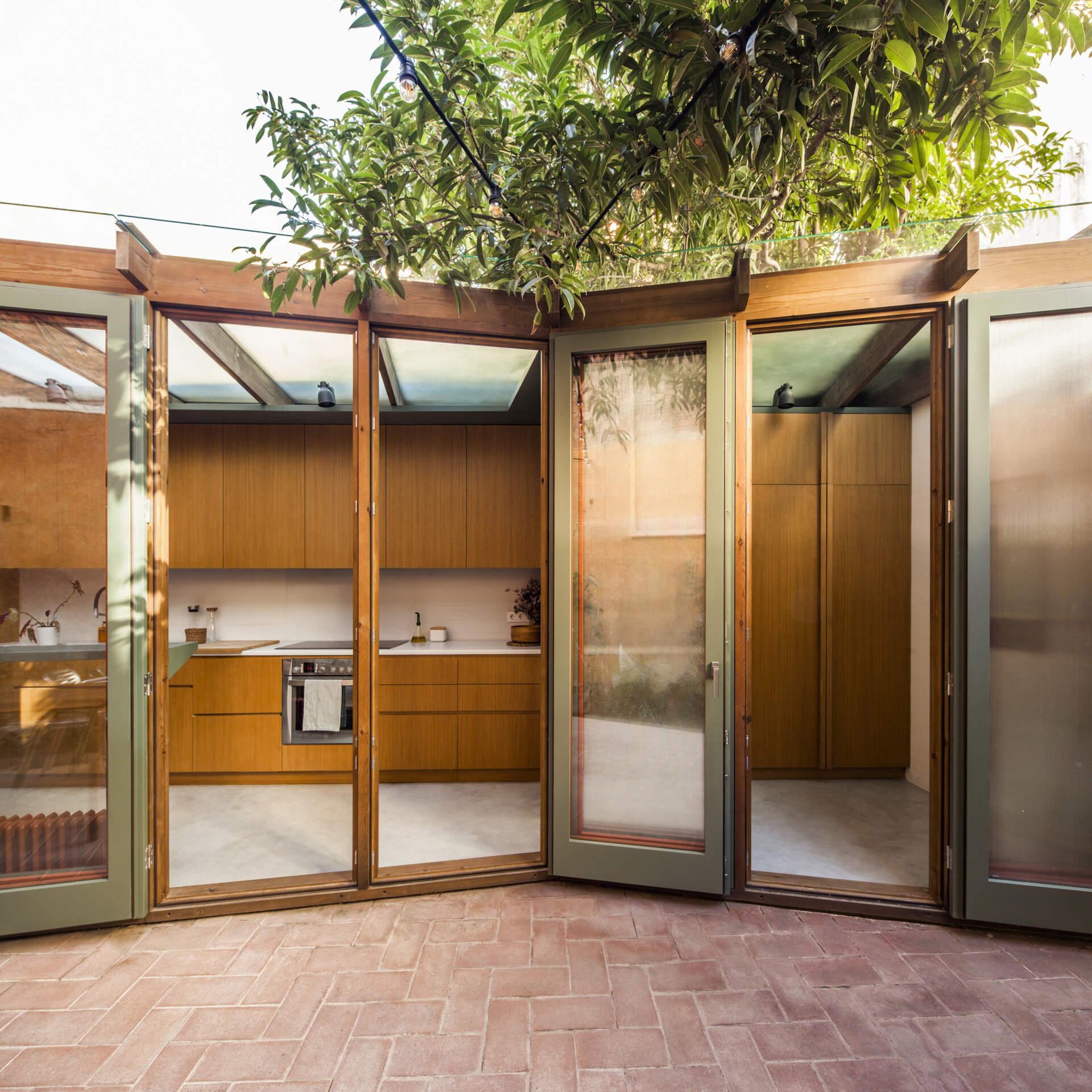 This house extension is conceived almost entirely as a transparent structure, built with wood and glass in the spirit of a greenhouse. Rather than blocking light, the glazed facade ensures that natural illumination continues to filter through the rest of the ground floor.