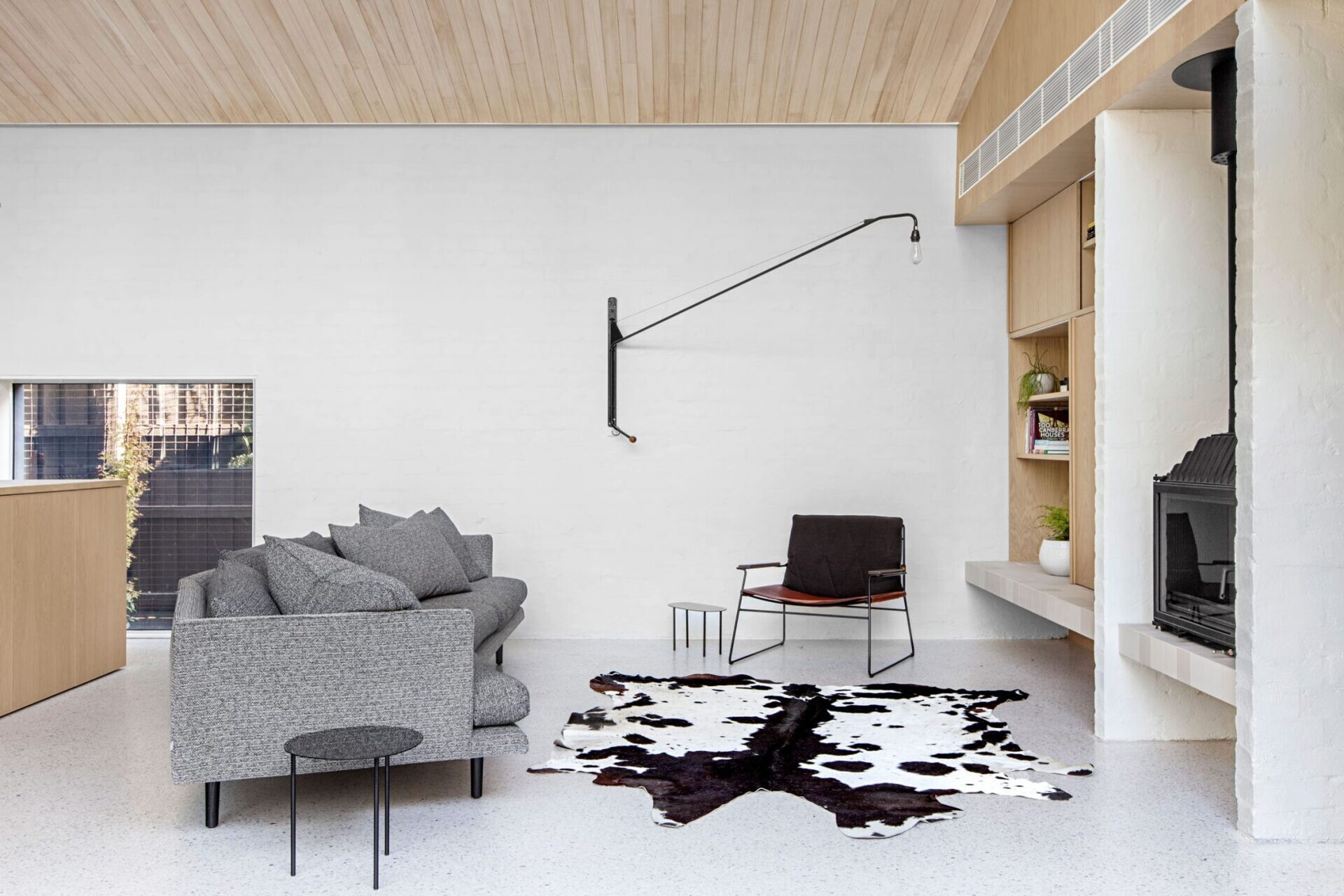 A curved grey sofa faces a black fireplace, paired with a wood bookshelf and industrial lighting.