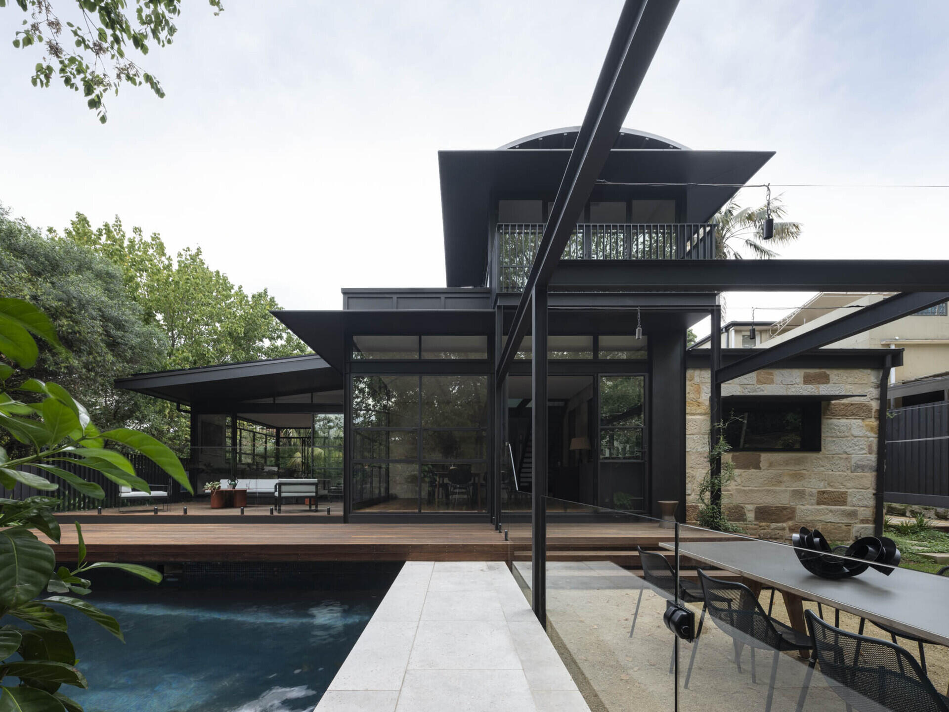 Steel-framed glazing leads to sheltered zones that frame leafy views while the refurbished pool made outdoor living part of the daily experience.
