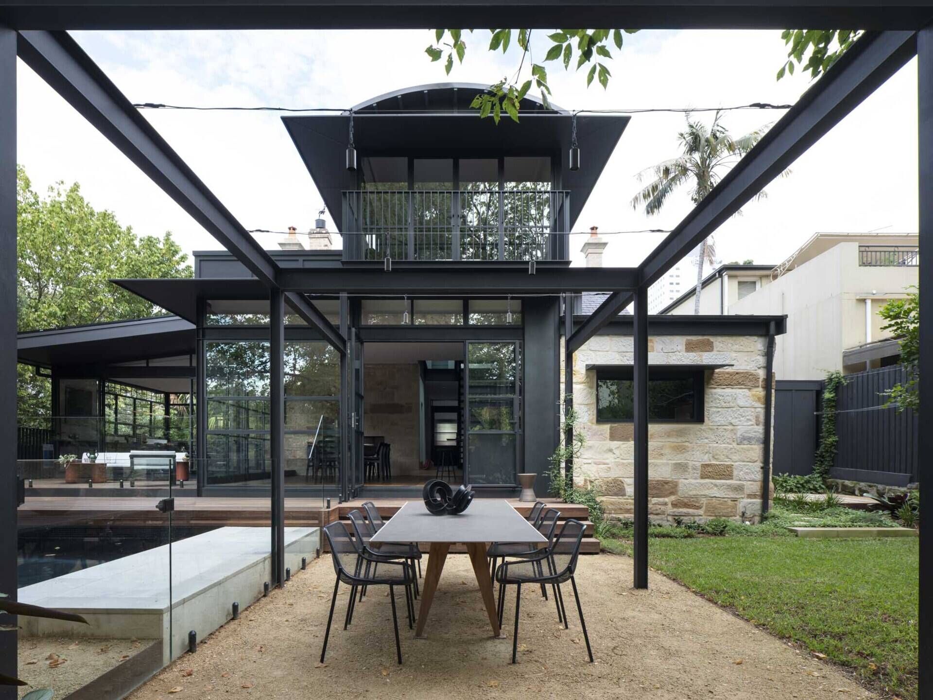 Steel-framed glazing leads to sheltered zones that frame leafy views while the refurbished pool made outdoor living part of the daily experience.