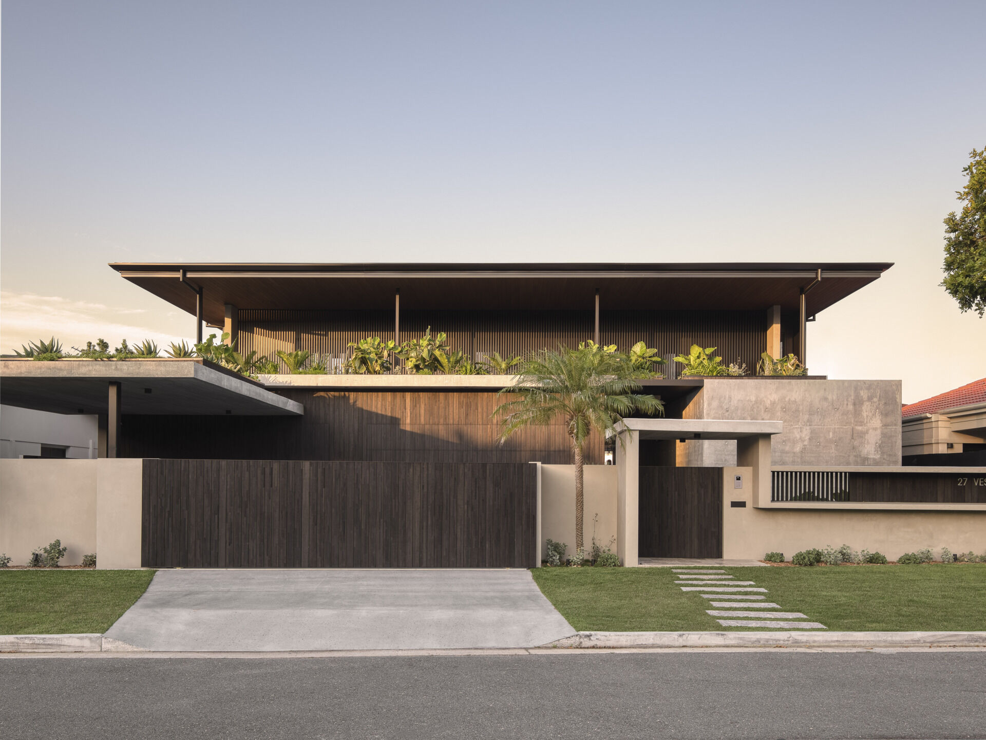 The western facade makes a bold first impression. Its monolithic form shields the home from the harsh afternoon sun while sculpting a striking architectural identity. Deep overhangs and battened screens soften the edges, while rooftop gardens introduce greenery at every level.