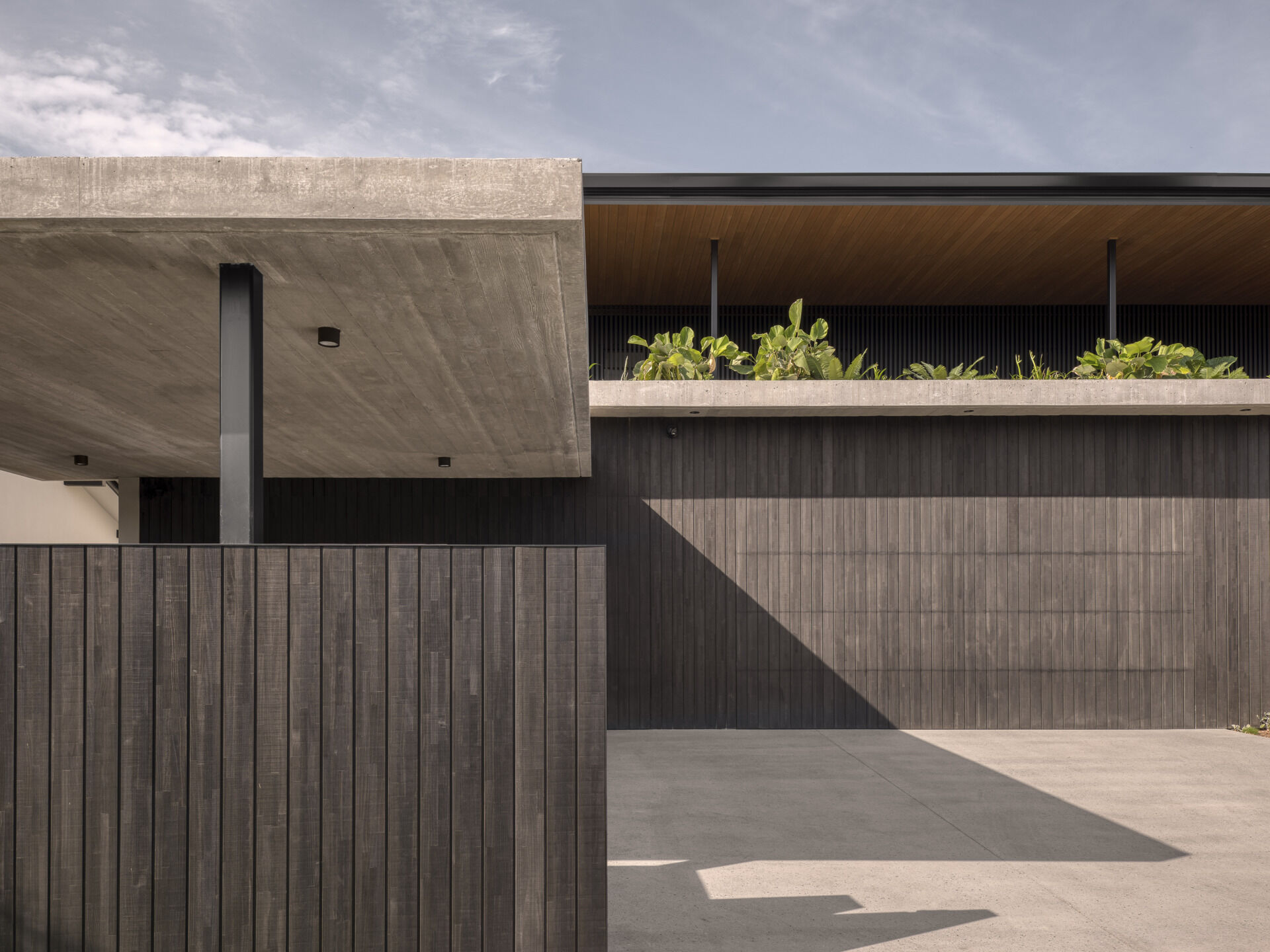 The western facade makes a bold first impression. Its monolithic form shields the home from the harsh afternoon sun while sculpting a striking architectural identity. Deep overhangs and battened screens soften the edges, while rooftop gardens introduce greenery at every level.