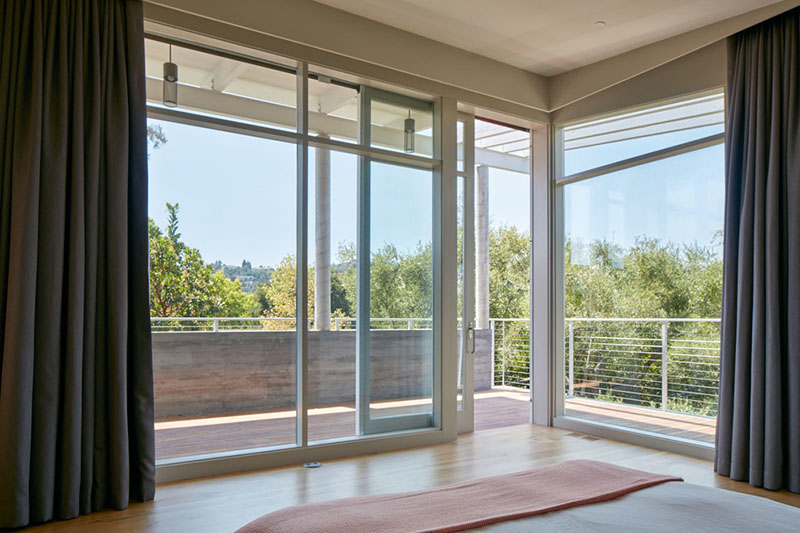 This master suite has its own vestibule lined with storage and lit by a skylight. The bedroom itself features expansive floor-to-ceiling windows and sliding doors that open to a covered porch.