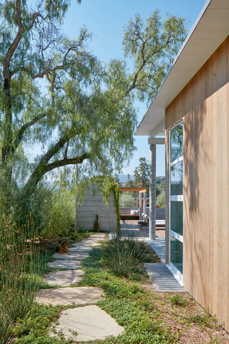 Since this home sits on a sloped site, landscaped paths guide movement across the property. Large stepping stones framed by ground cover create a garden-like walkway to the pool. Elsewhere, a dedicated firepit area invites gatherings around the warmth of an open flame.