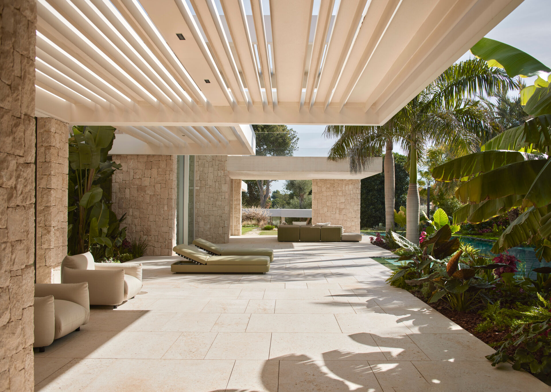 Outdoors at this modern home, the swimming pool becomes more than just a place to cool off. Its long reflective surface mirrors the garden around it, visually extending the landscape, while the patio has various seating areas with some covered. At the same time, it naturally lowers the temperature, helping create a cooler atmosphere across the outdoor areas.