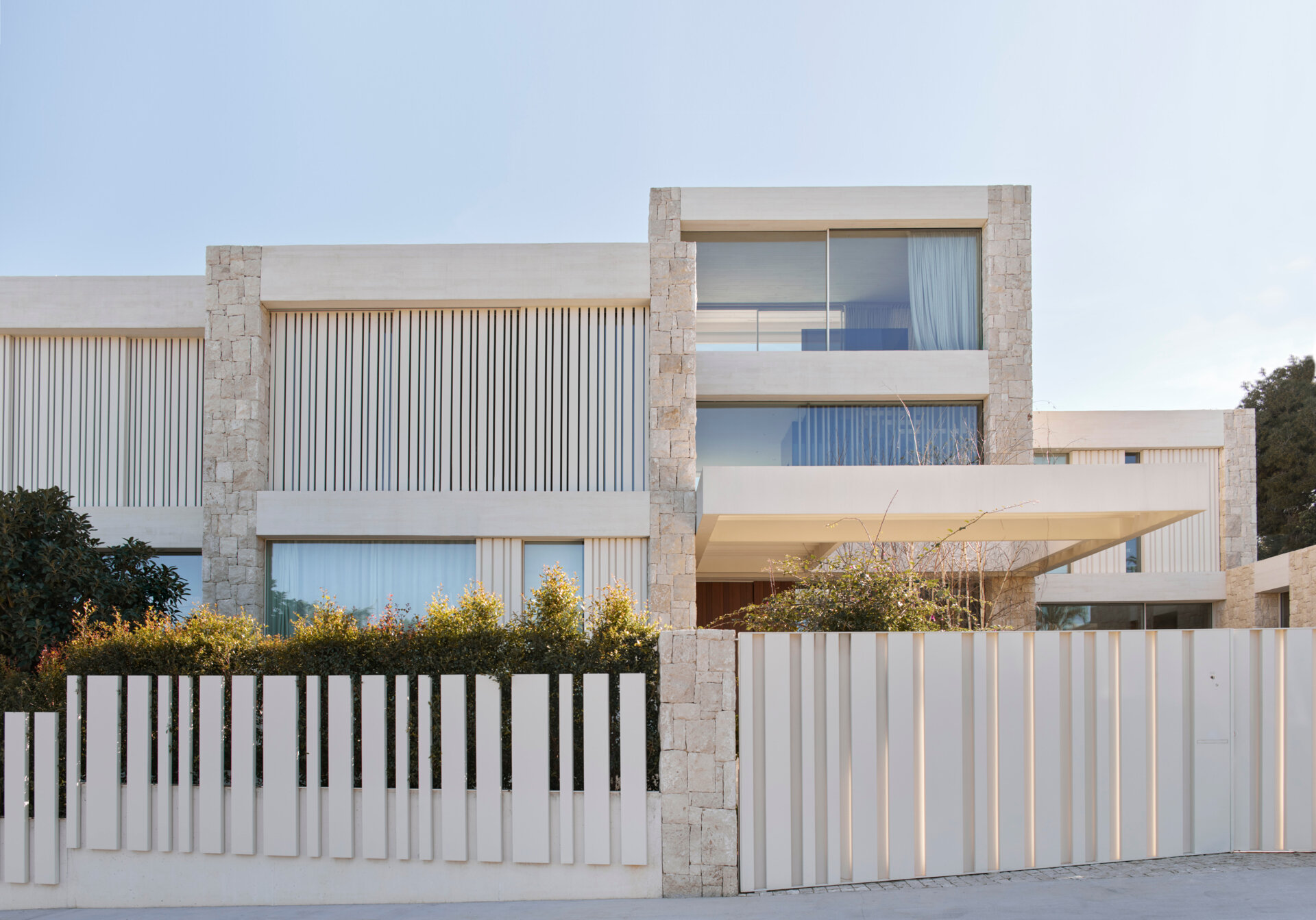 Stone, white concrete, and steel define the exterior of this modern home, softened by light woods inside.