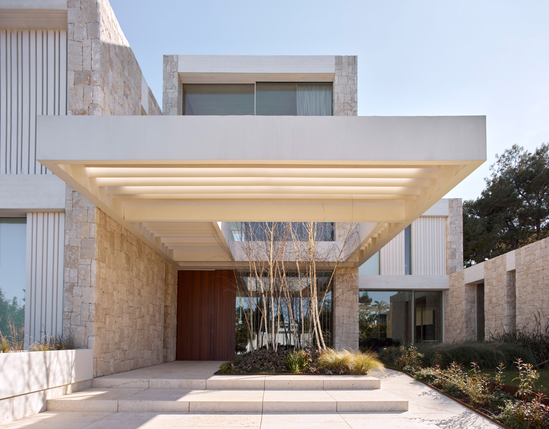 Stone, white concrete, and steel define the exterior of this modern home, softened by light woods inside.