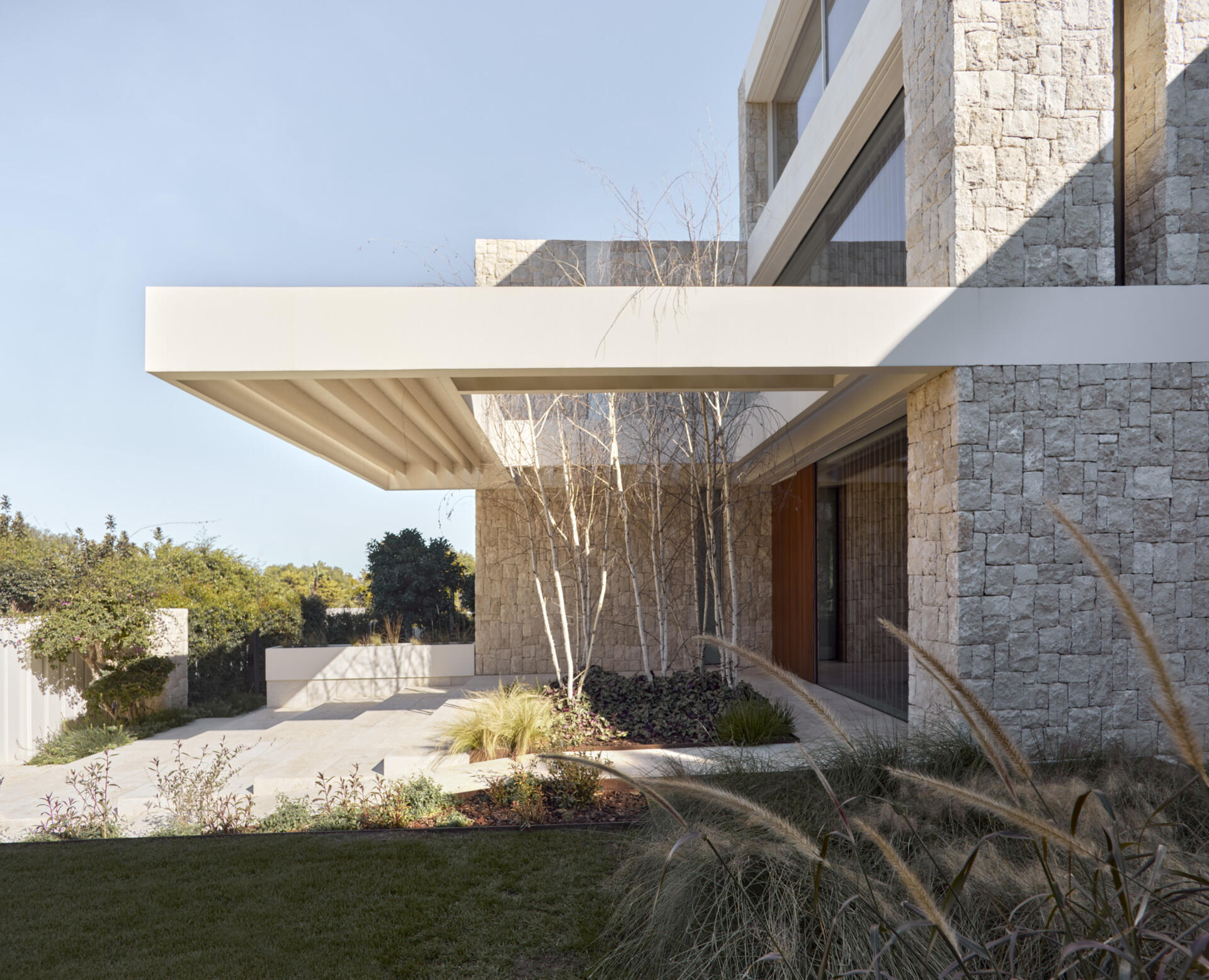 Stone, white concrete, and steel define the exterior of this modern home, softened by light woods inside.