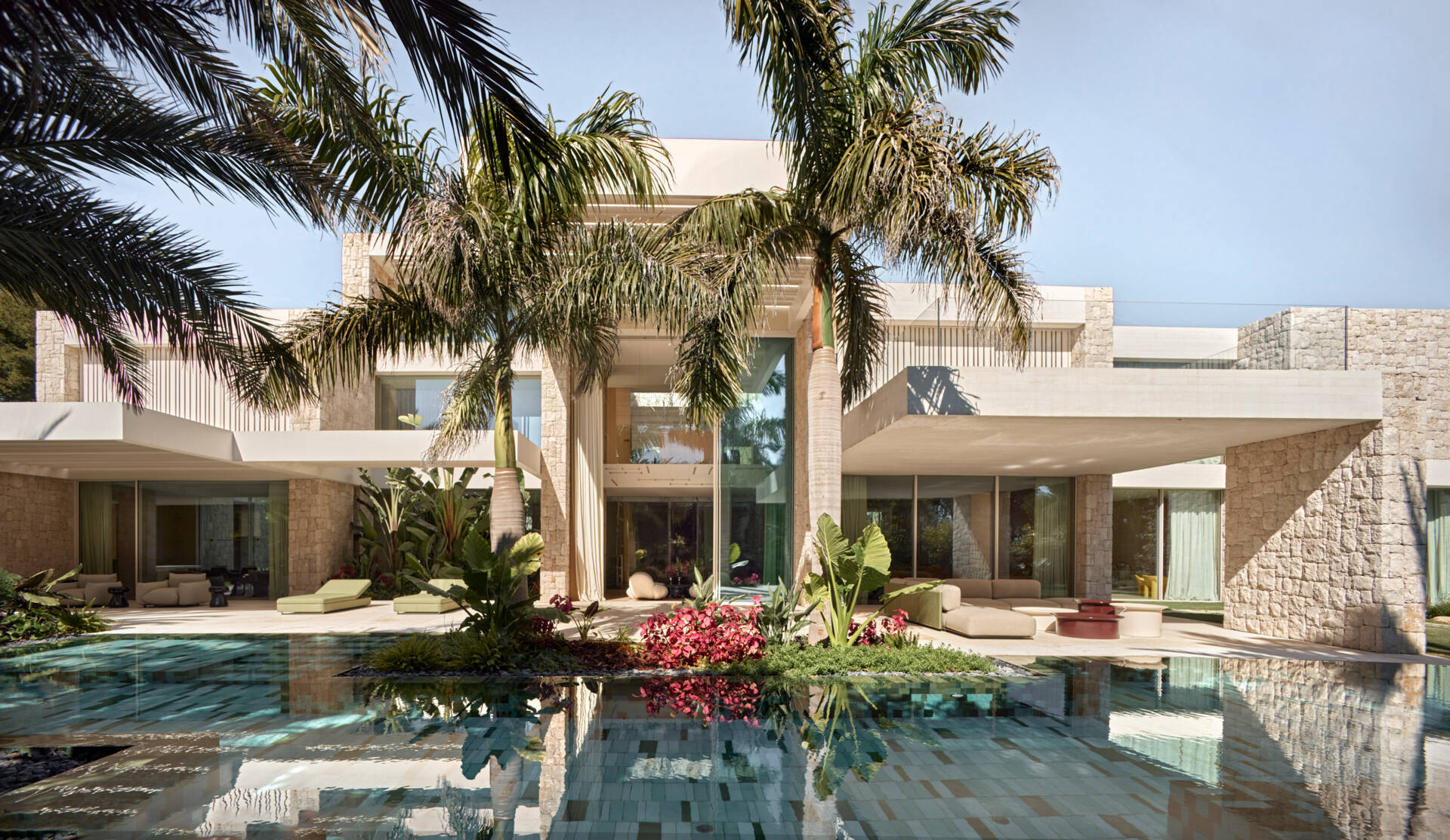 Outdoors at this modern home, the swimming pool becomes more than just a place to cool off. Its long reflective surface mirrors the garden around it, visually extending the landscape, while the patio has various seating areas with some covered. At the same time, it naturally lowers the temperature, helping create a cooler atmosphere across the outdoor areas.