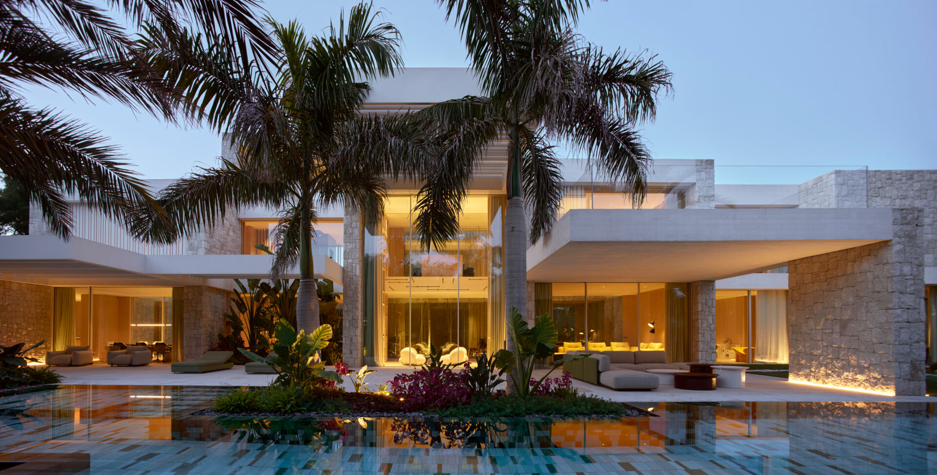 Outdoors at this modern home, the swimming pool becomes more than just a place to cool off. Its long reflective surface mirrors the garden around it, visually extending the landscape, while the patio has various seating areas with some covered. At the same time, it naturally lowers the temperature, helping create a cooler atmosphere across the outdoor areas.