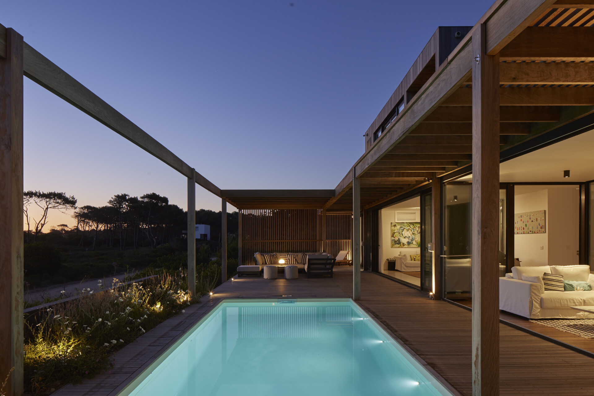 This prefabricated modular house, clad in wood, has a swimming pool, and preserves the sandy terrain while opening all rooms toward the sea.