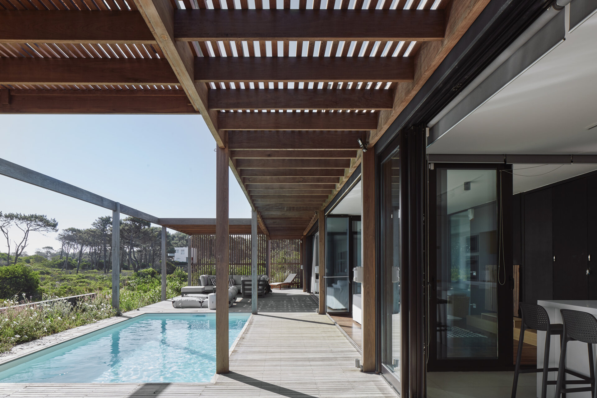 This prefabricated modular house, clad in wood, has a swimming pool, and preserves the sandy terrain while opening all rooms toward the sea.