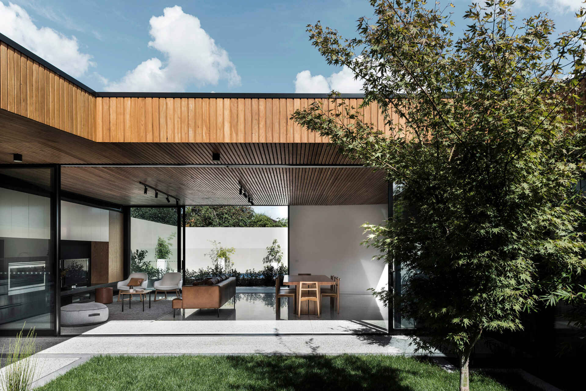 The interiors are designed with contrast in mind. A timber batten ceiling draws the eye through the space, guiding movement while warming the atmosphere. Below, white concrete flooring keeps the rooms light and airy. In the living area, a black feature wall defines the space within the open-plan layout, balancing the softer tones of wood and brick.