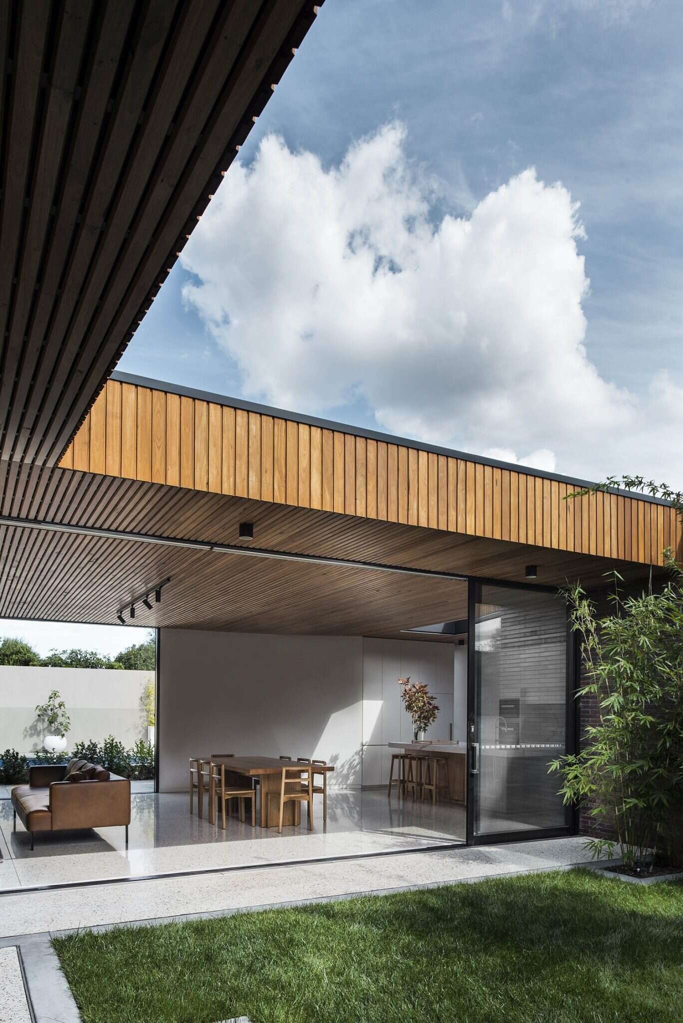 The interiors are designed with contrast in mind. A timber batten ceiling draws the eye through the space, guiding movement while warming the atmosphere. Below, white concrete flooring keeps the rooms light and airy. In the living area, a black feature wall defines the space within the open-plan layout, balancing the softer tones of wood and brick.