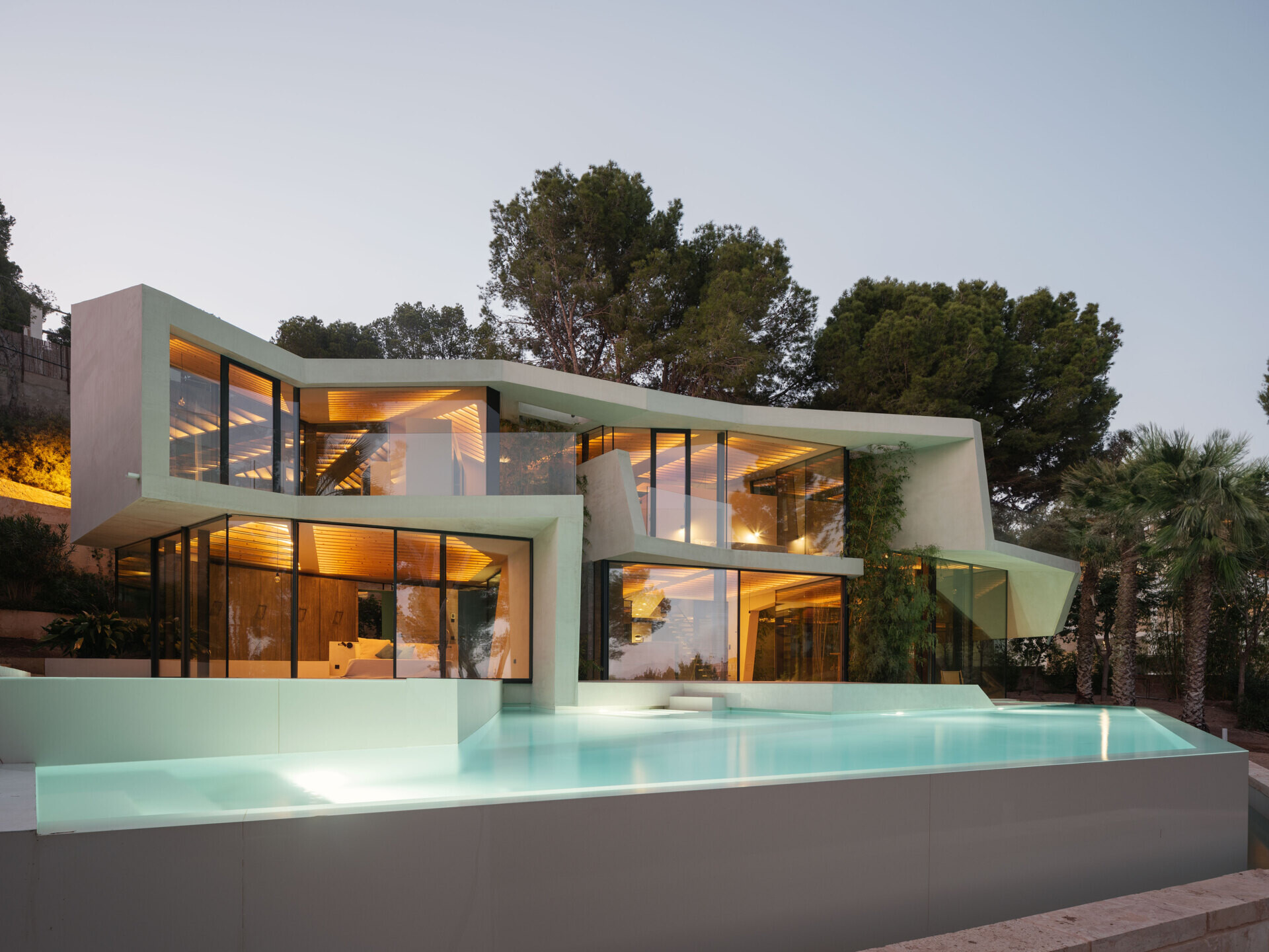 A hillside pool in Paguera frames the pine canopy and bay views, turning water and glass into a seamless extension of the home’s design.