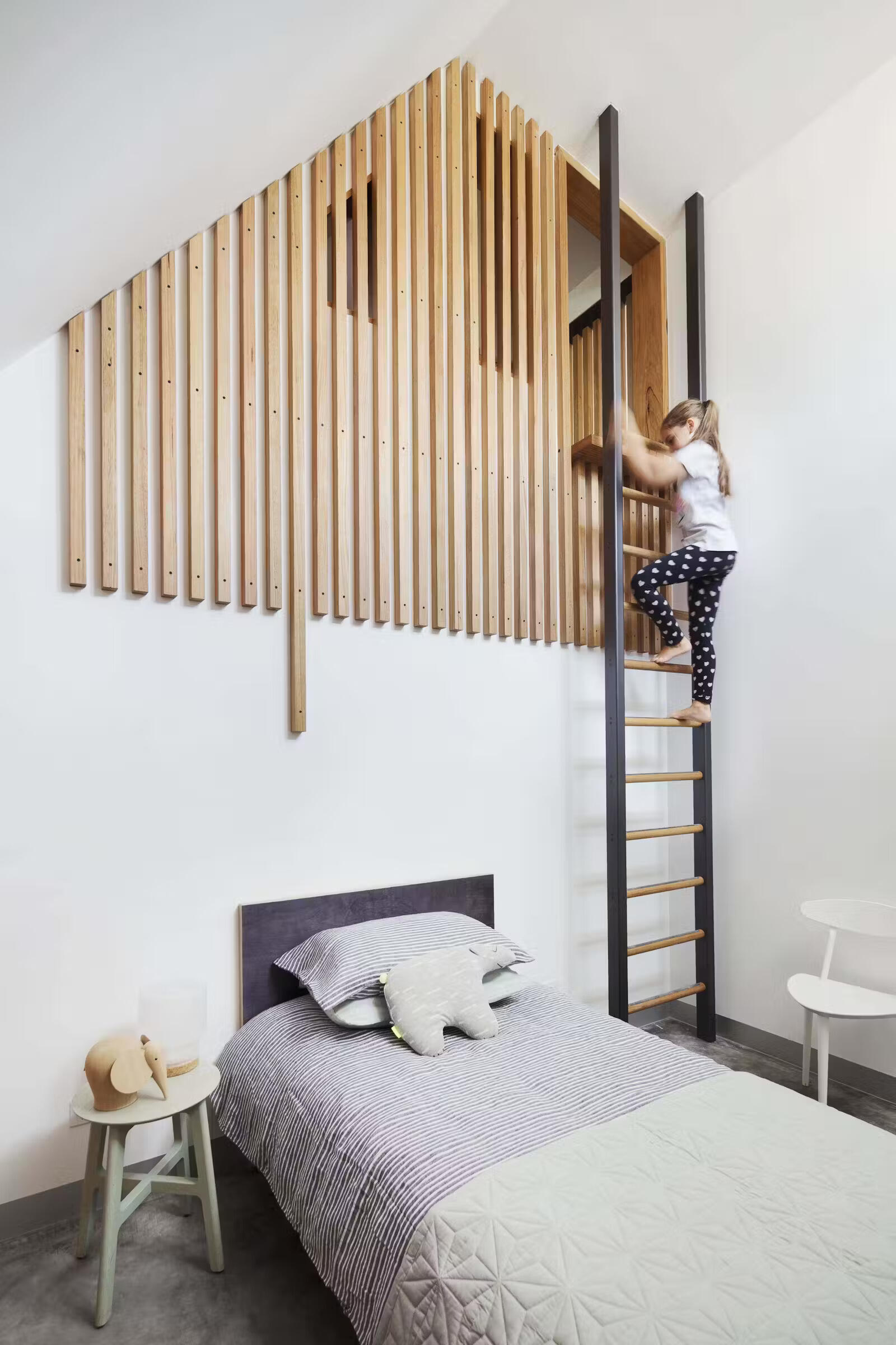 Wood slats form a bedroom wall, hiding a loft above and creating a layered, architectural effect.