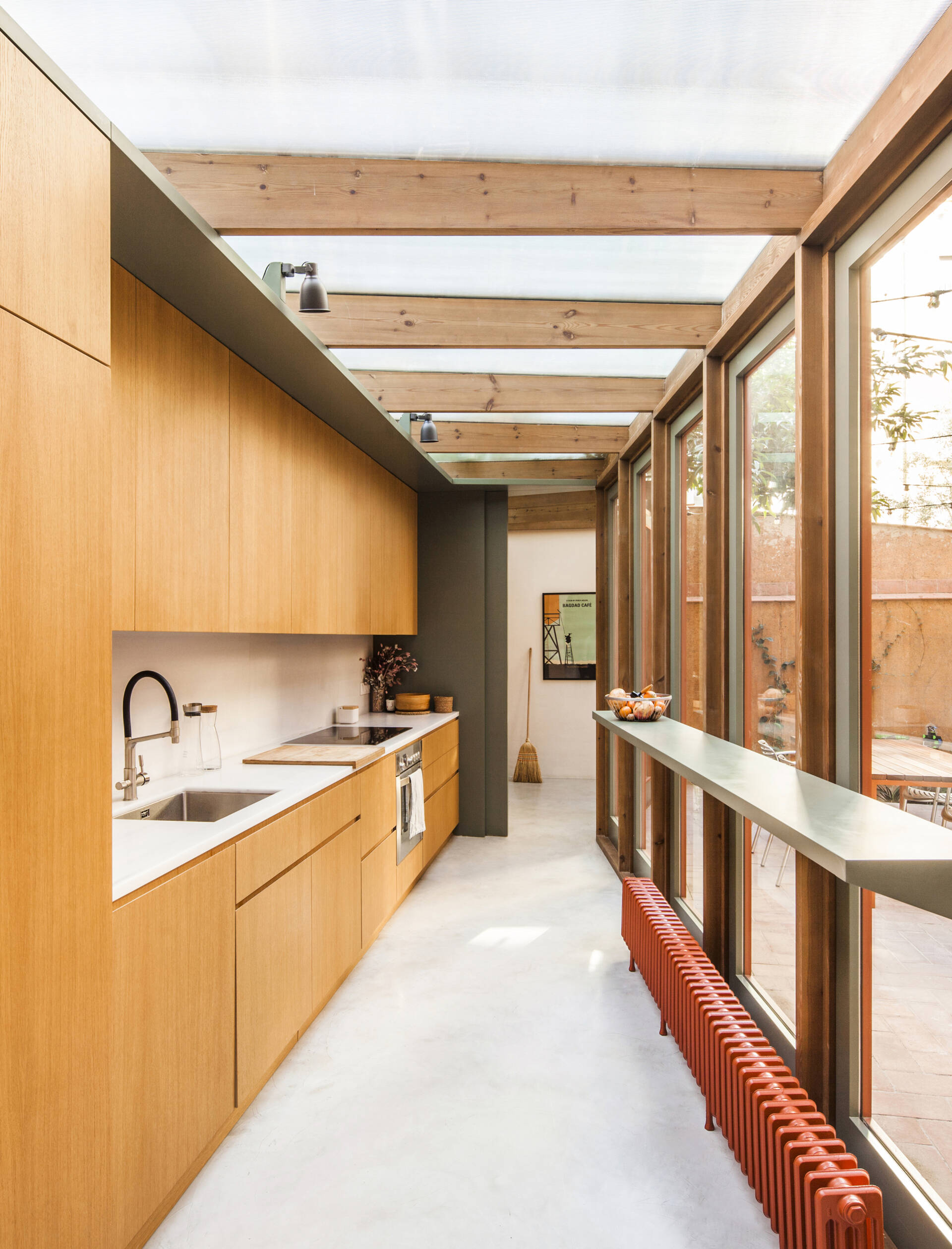 In this renovated house, the kitchen cabinets are crafted in warm wood with a clean, hardware free design that emphasizes simplicity and function. Running along one wall, the cabinetry keeps storage discreet while creating a continuous visual rhythm.