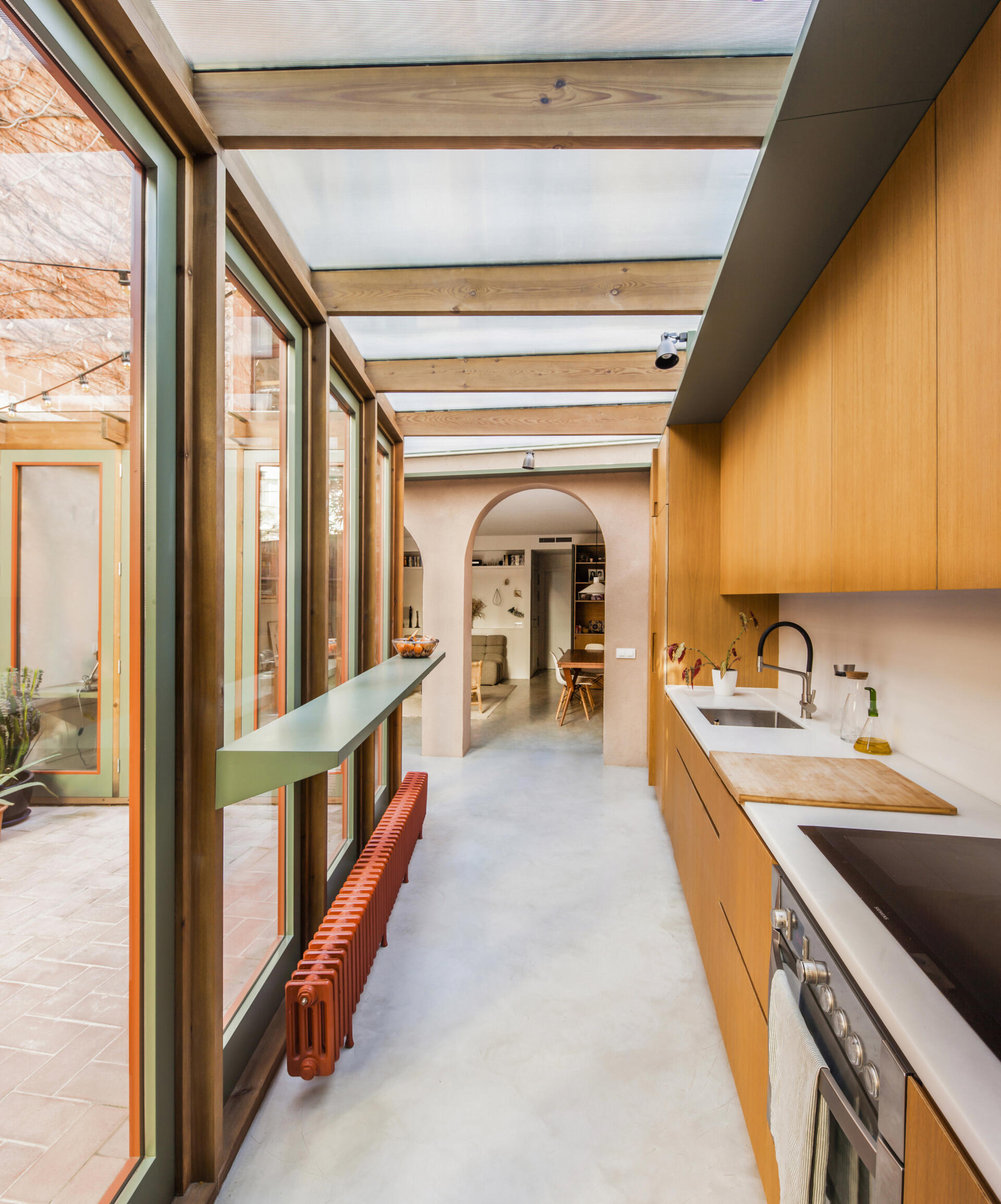 In this renovated house, the kitchen cabinets are crafted in warm wood with a clean, hardware free design that emphasizes simplicity and function. Running along one wall, the cabinetry keeps storage discreet while creating a continuous visual rhythm.